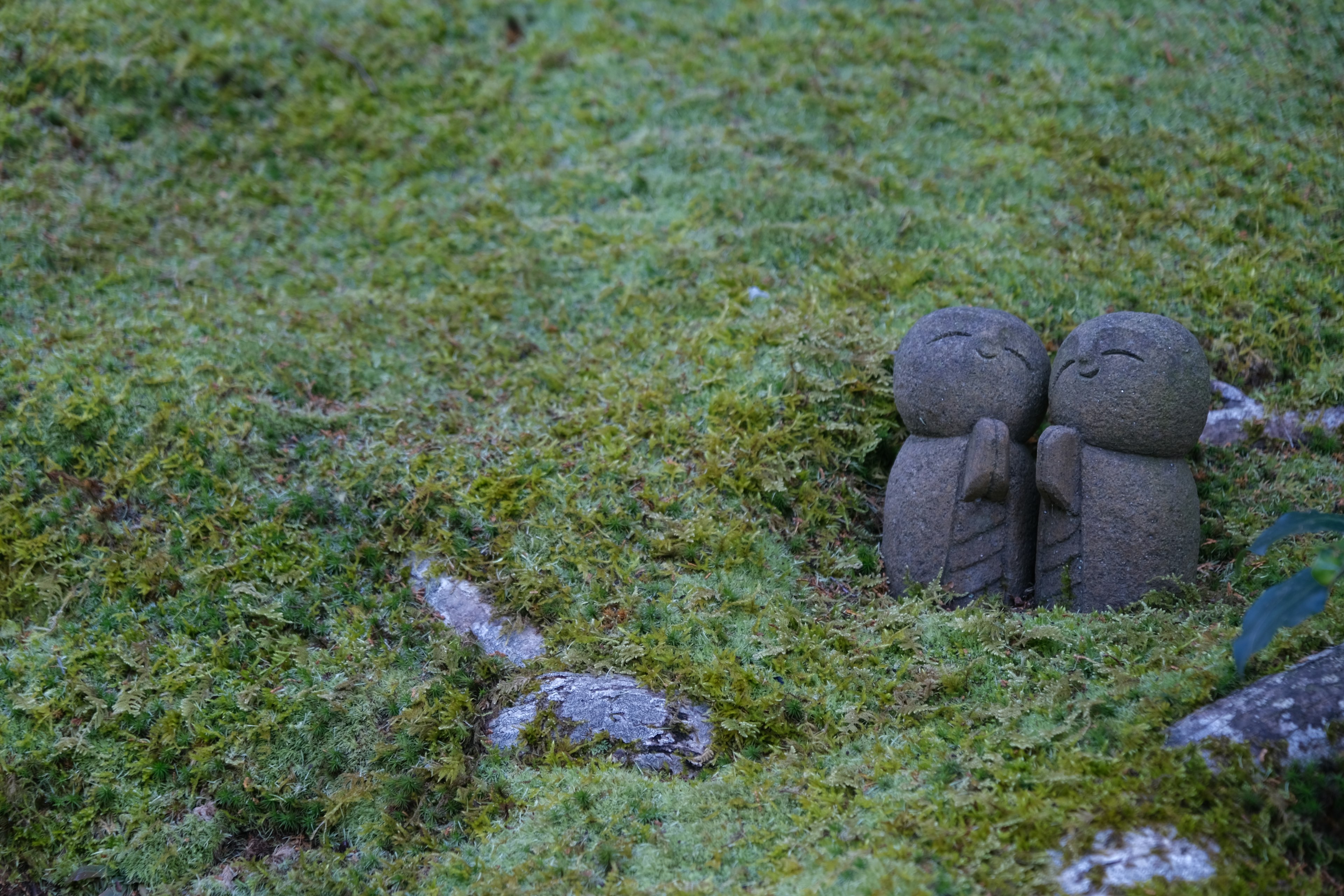 Dos pequeñas figuras de piedra en un suelo cubierto de musgo