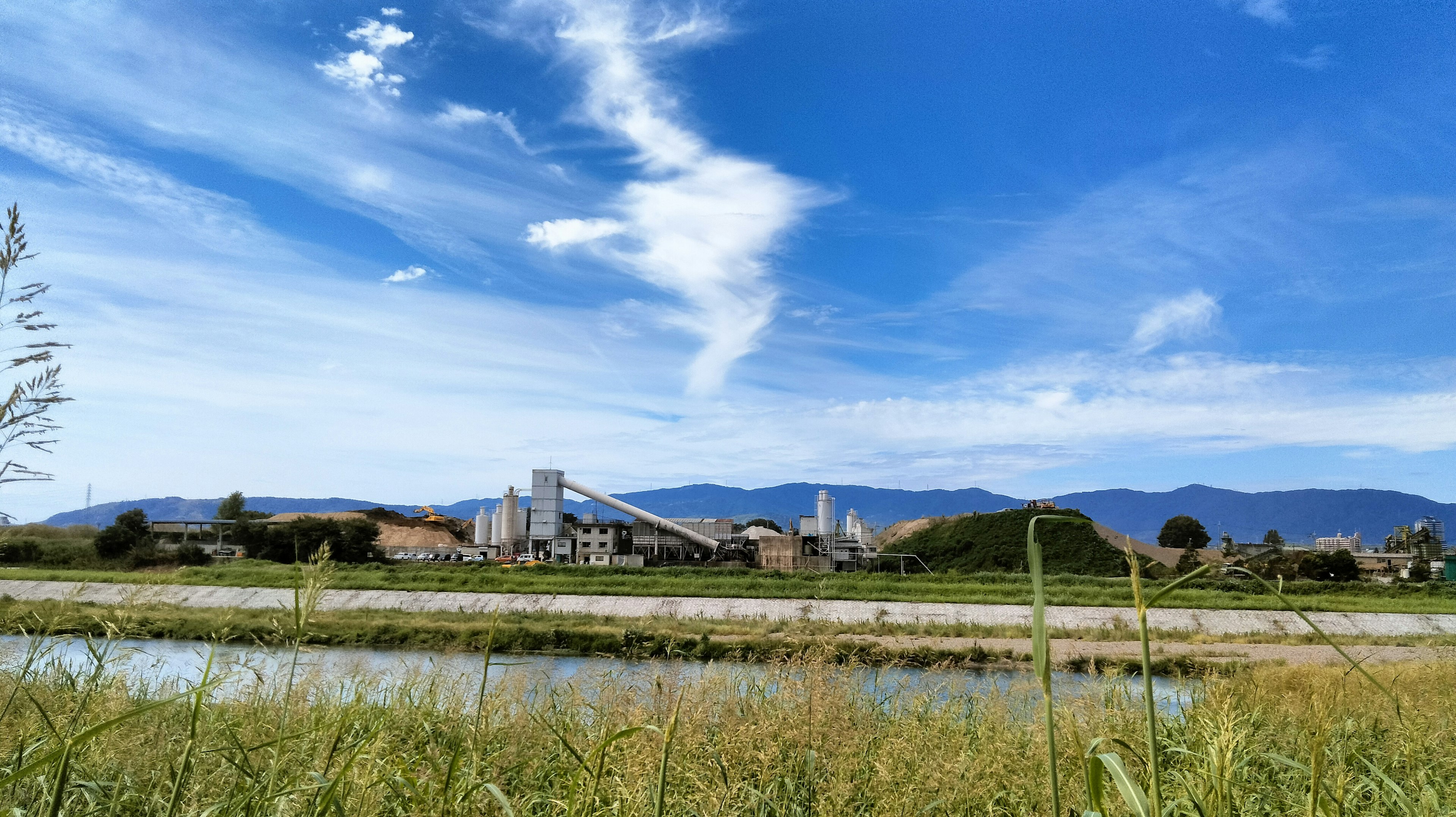 Fabriklandschaft unter einem blauen Himmel mit Wolken und einem ruhigen Fluss