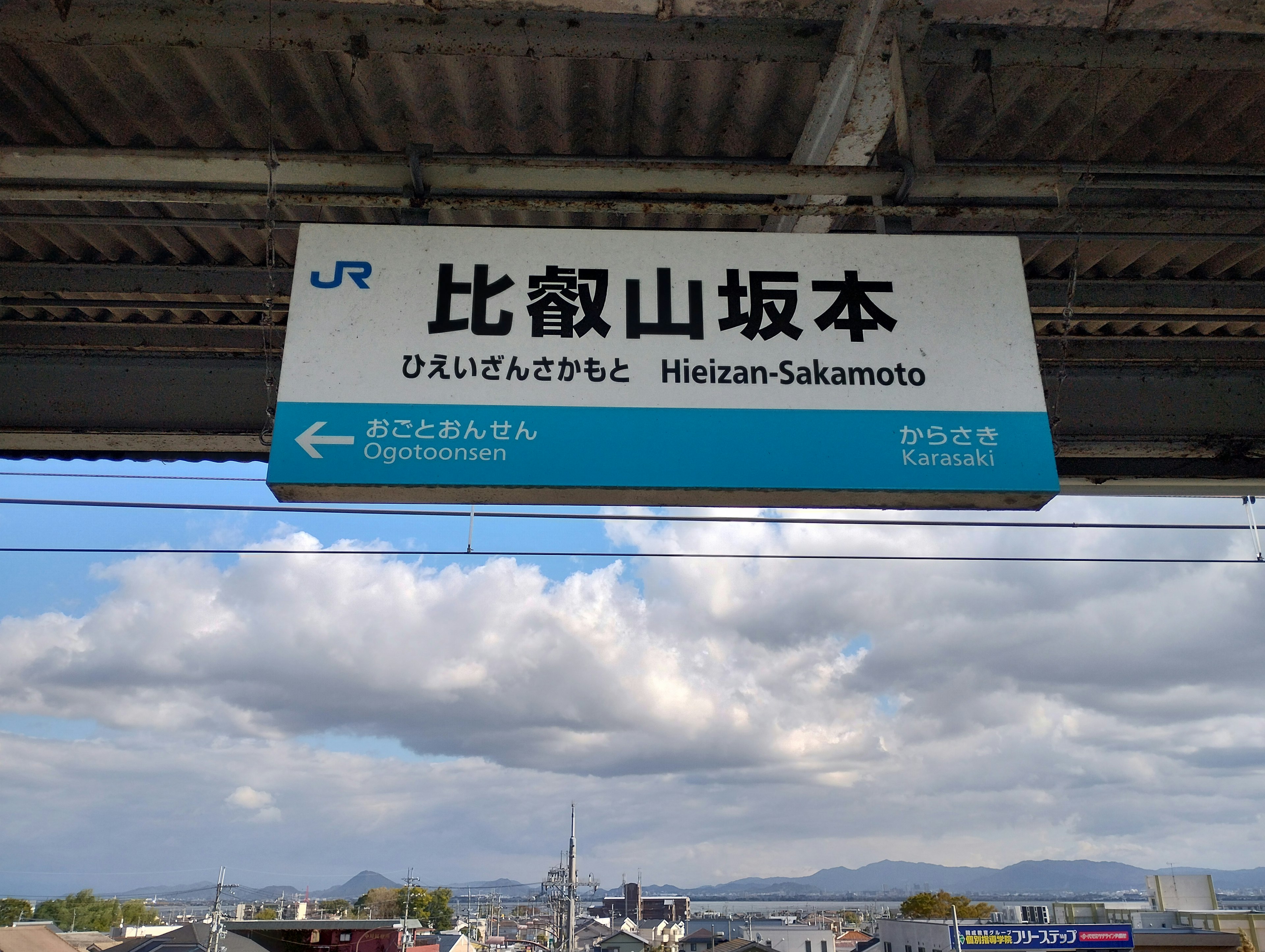 Insegna della stazione Heizan-Sakamoto con cielo blu e nuvole sullo sfondo