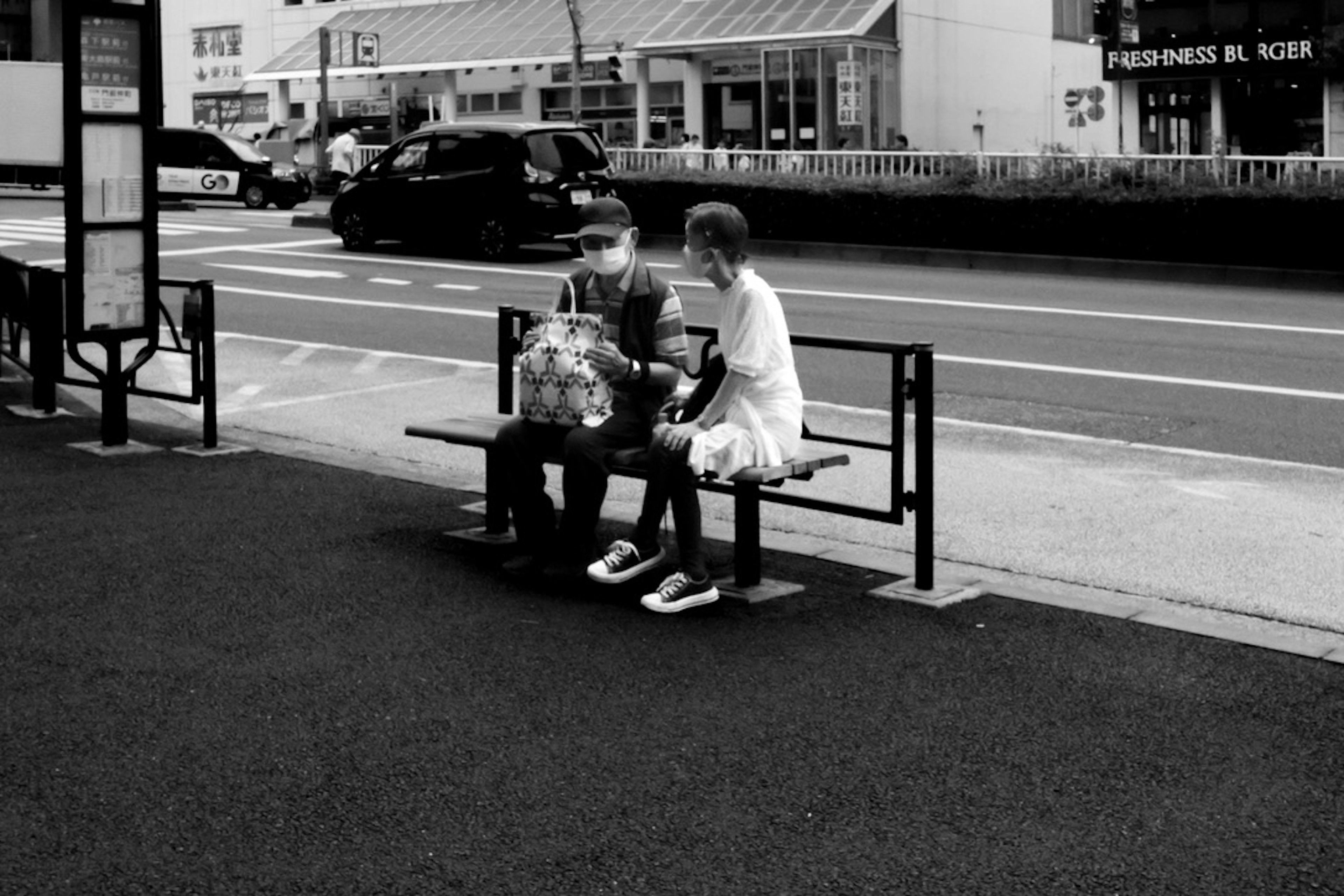 Black and white photo of a man and woman sitting at a bus stop