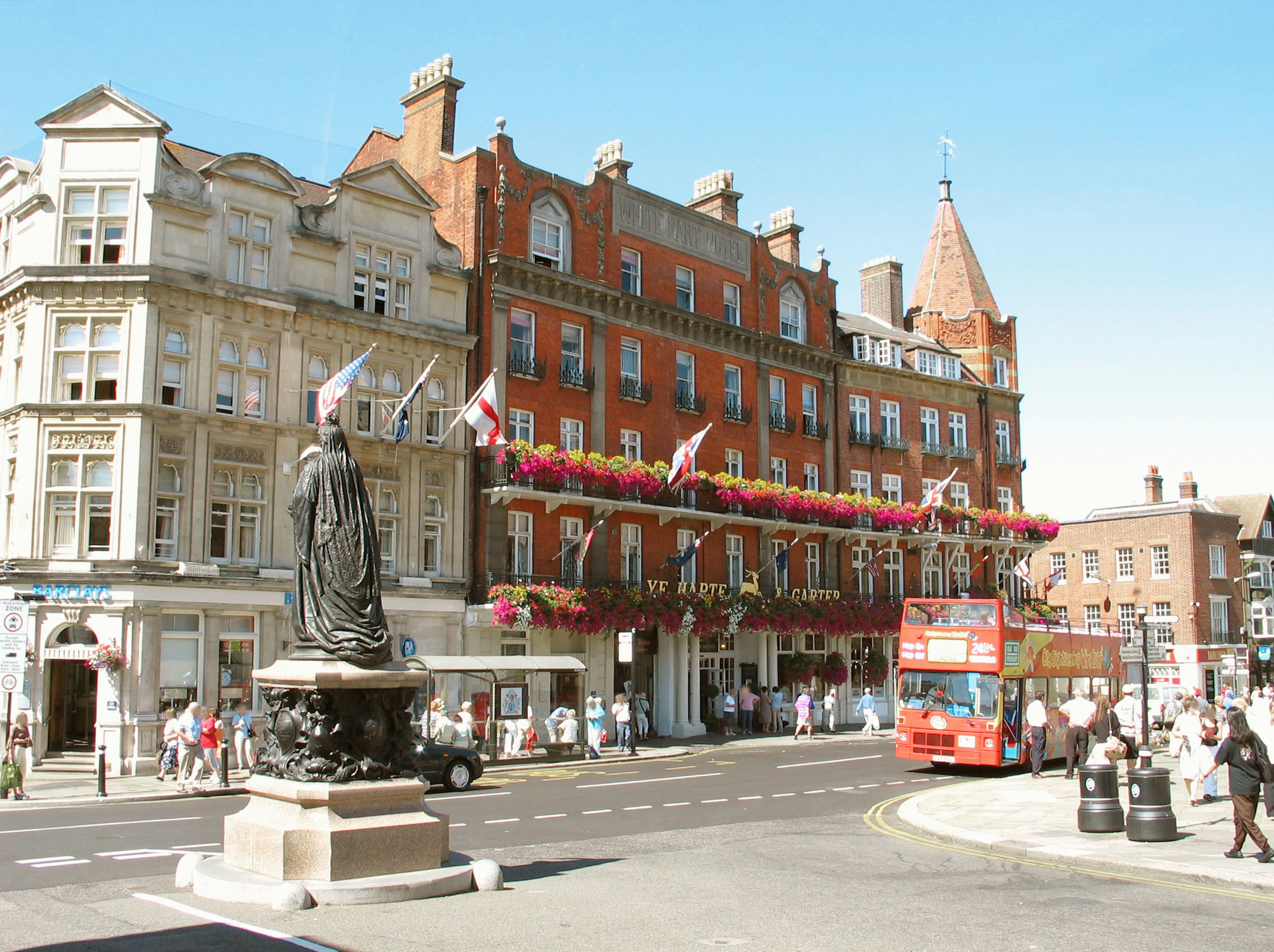 Estatua de una reina frente a edificios históricos con autobús rojo y decoraciones florales