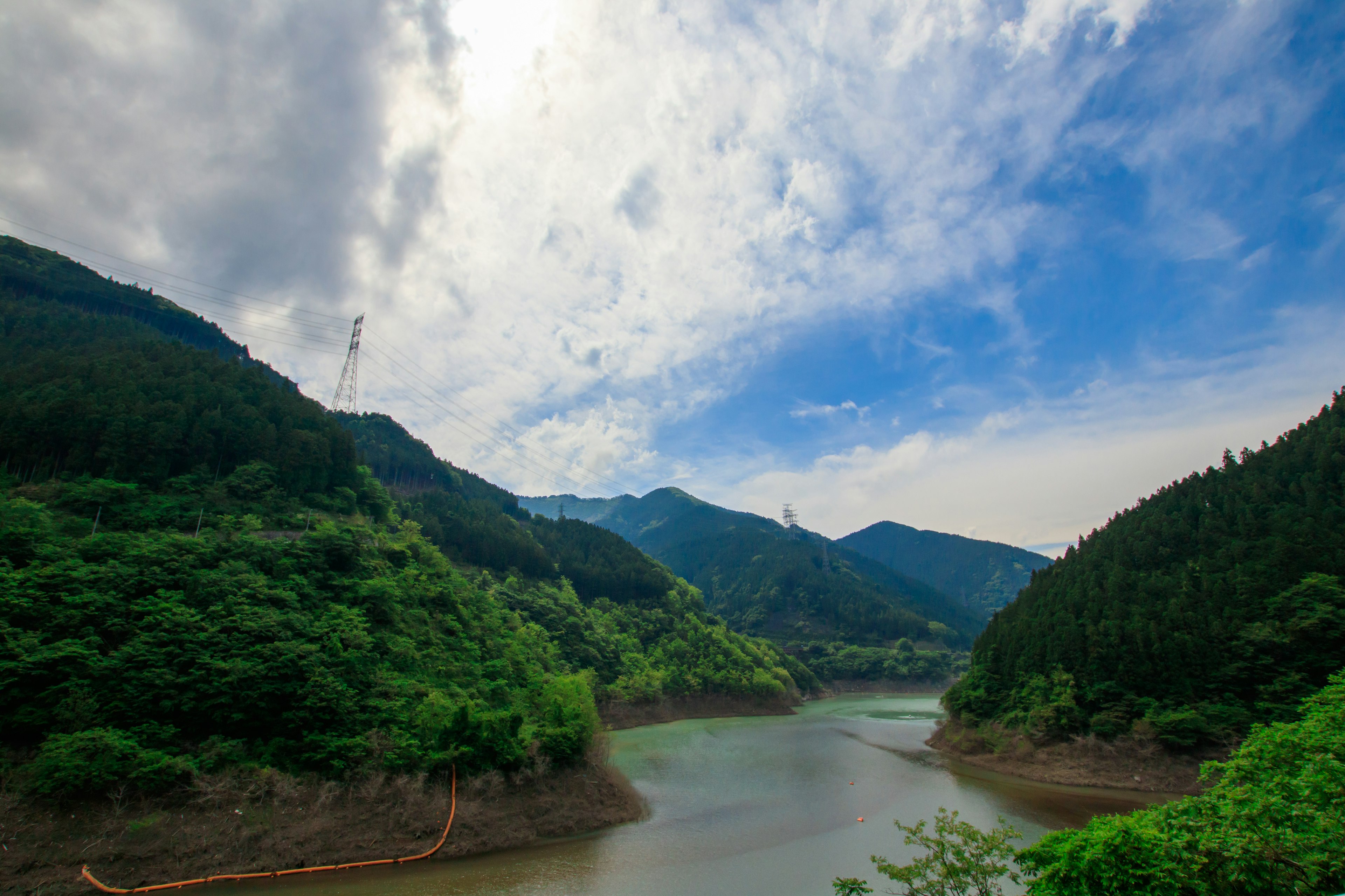 Danau tenang dikelilingi pegunungan subur langit biru cerah dengan awan yang tersebar