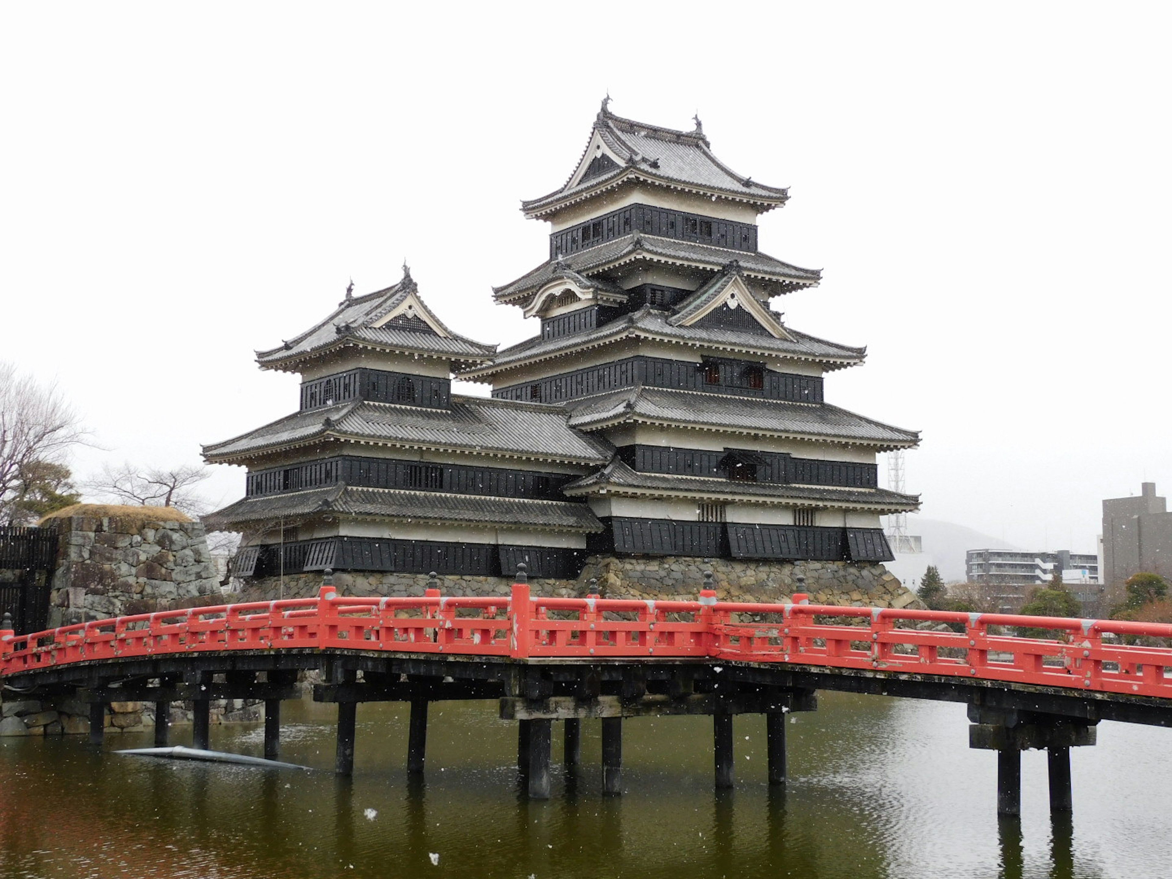 A historic black castle with multiple tiers and a red bridge over water