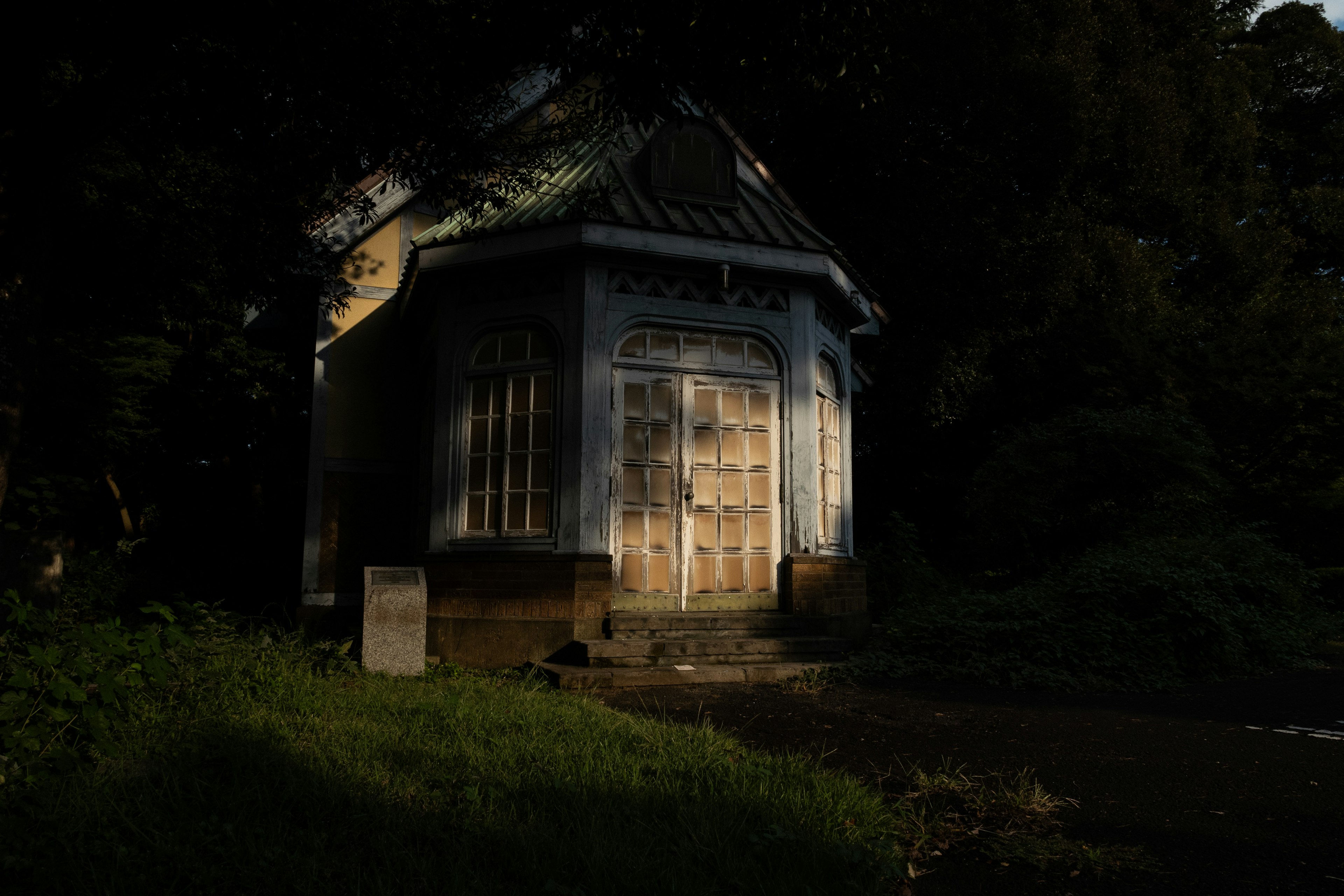 Un vecchio edificio in una foresta buia con luce che lo illumina parzialmente