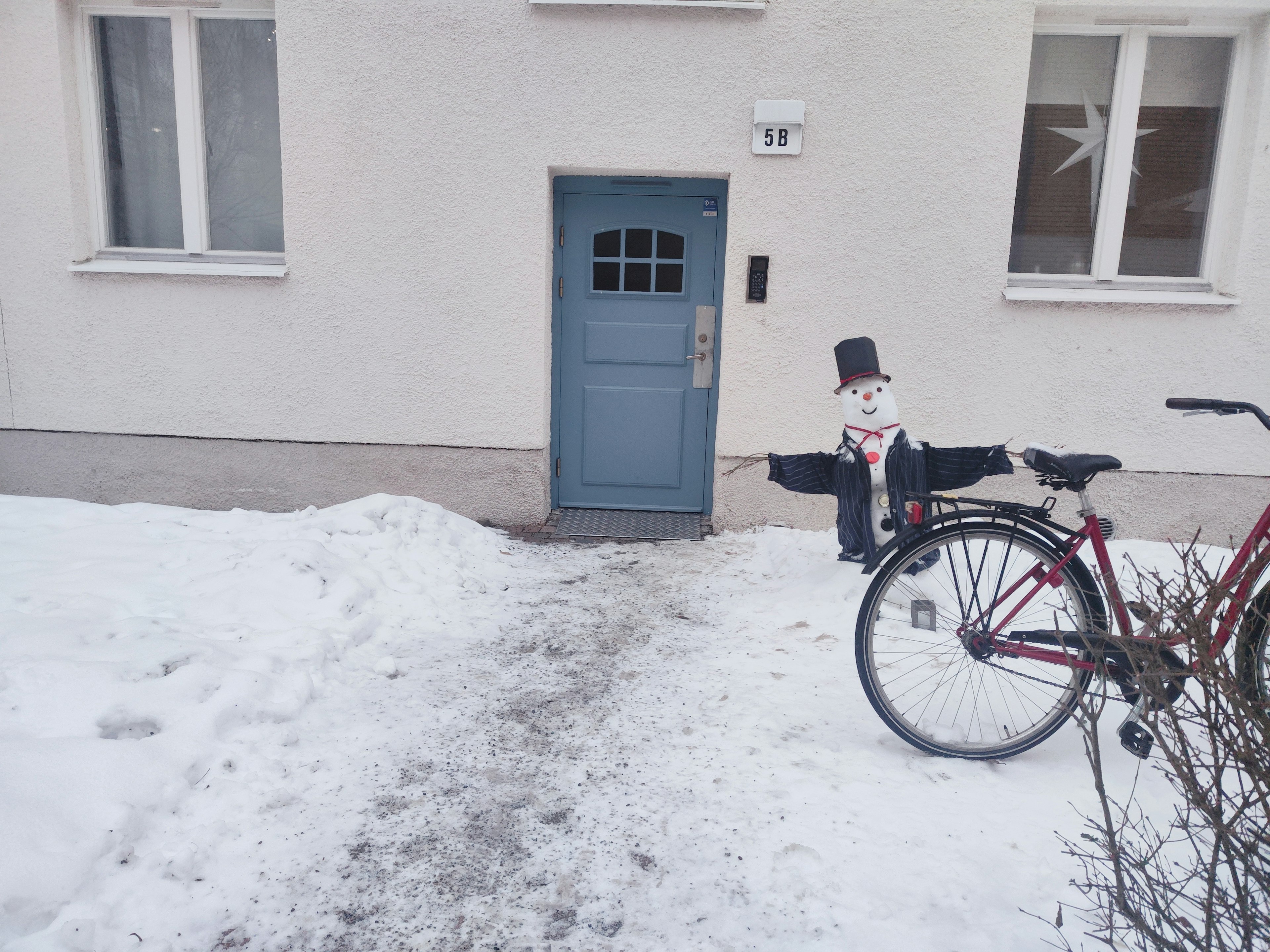 Ein Schneemann und ein Fahrrad vor einer blauen Tür, die mit Schnee bedeckt ist