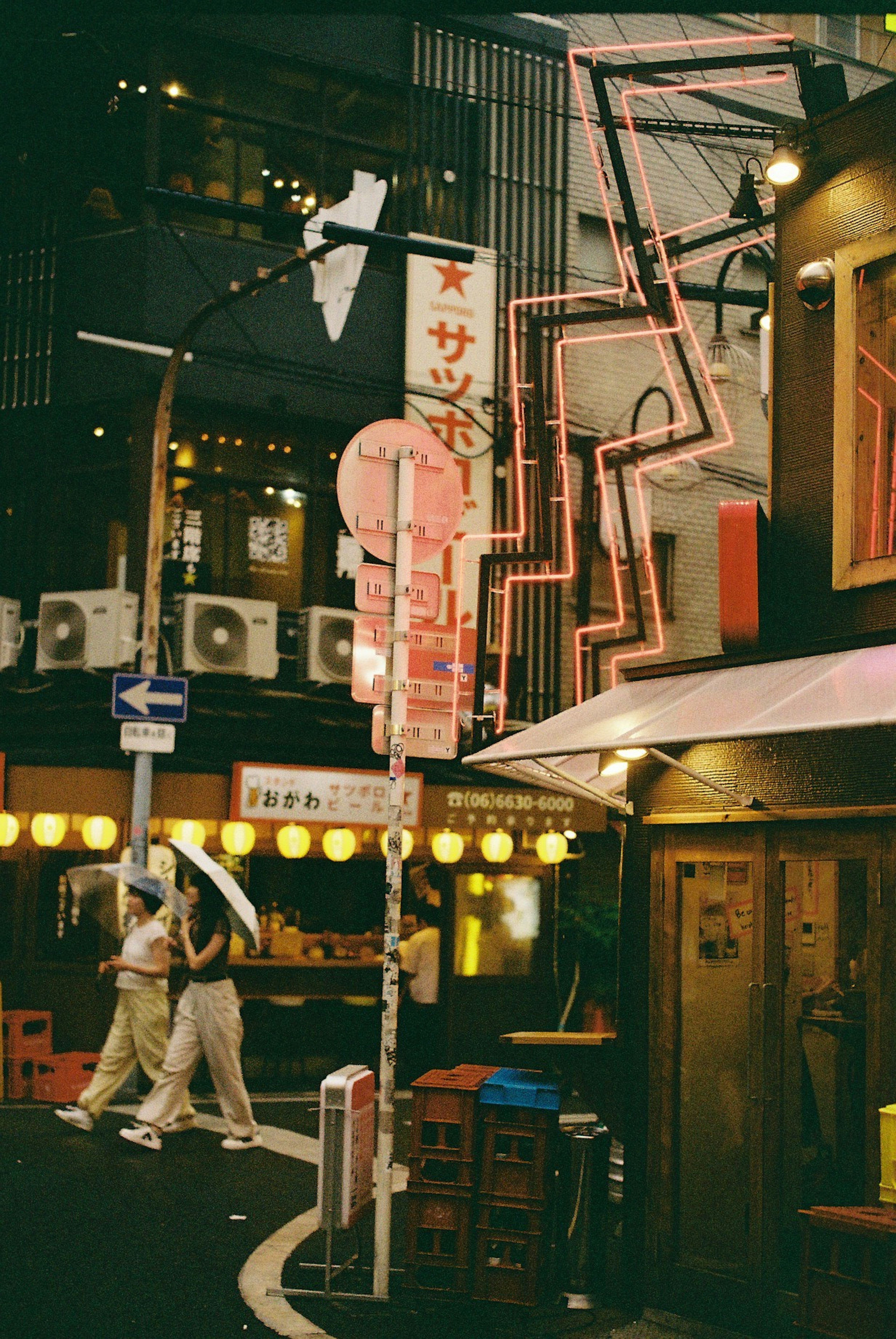 两个人在夜间街道上走，手持雨伞，背景有霓虹灯和灯笼