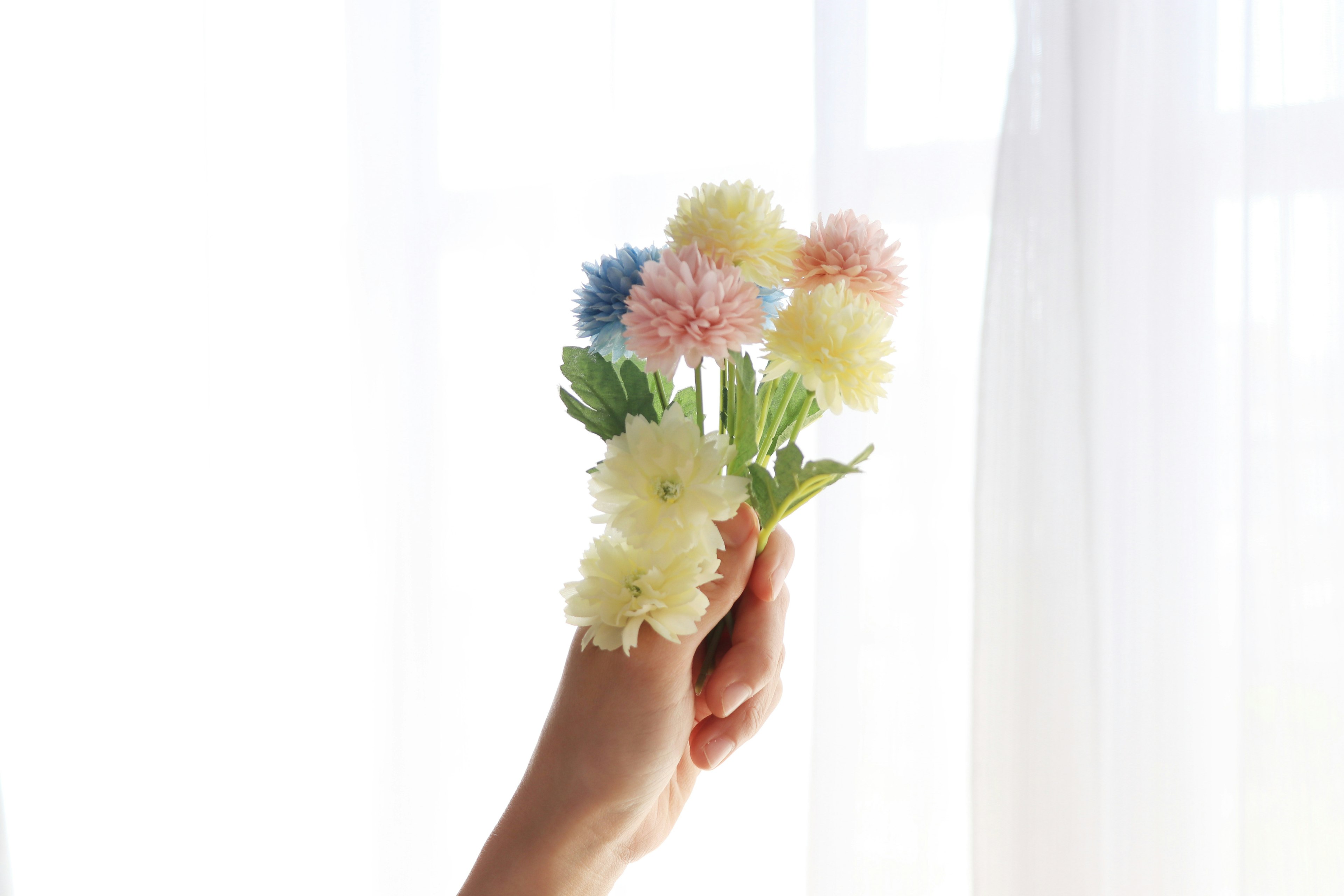 Eine Hand, die einen bunten Blumenstrauß hält, mit weichen Vorhängen im Hintergrund