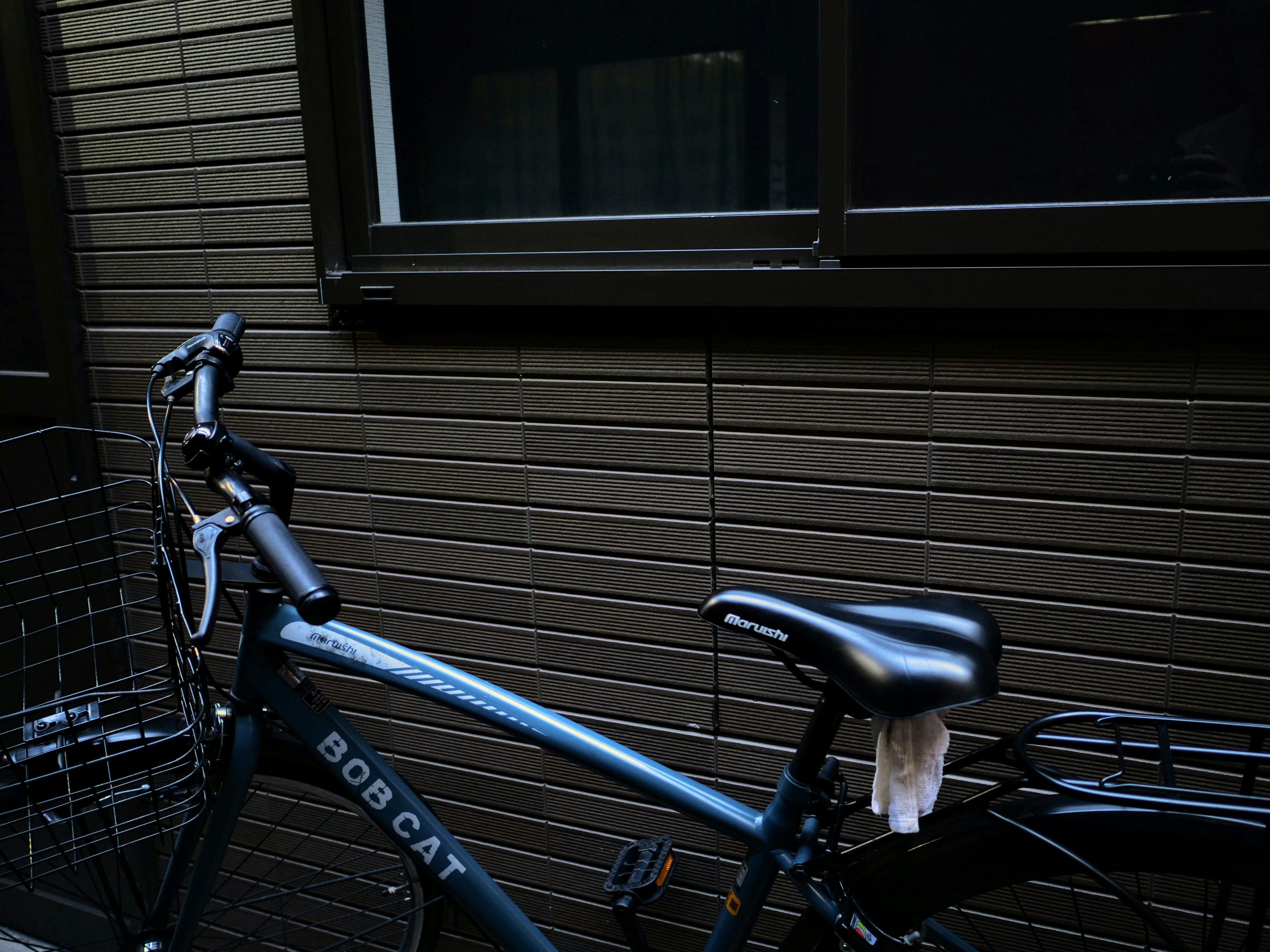 A blue bicycle parked beside a brown wall in a quiet setting