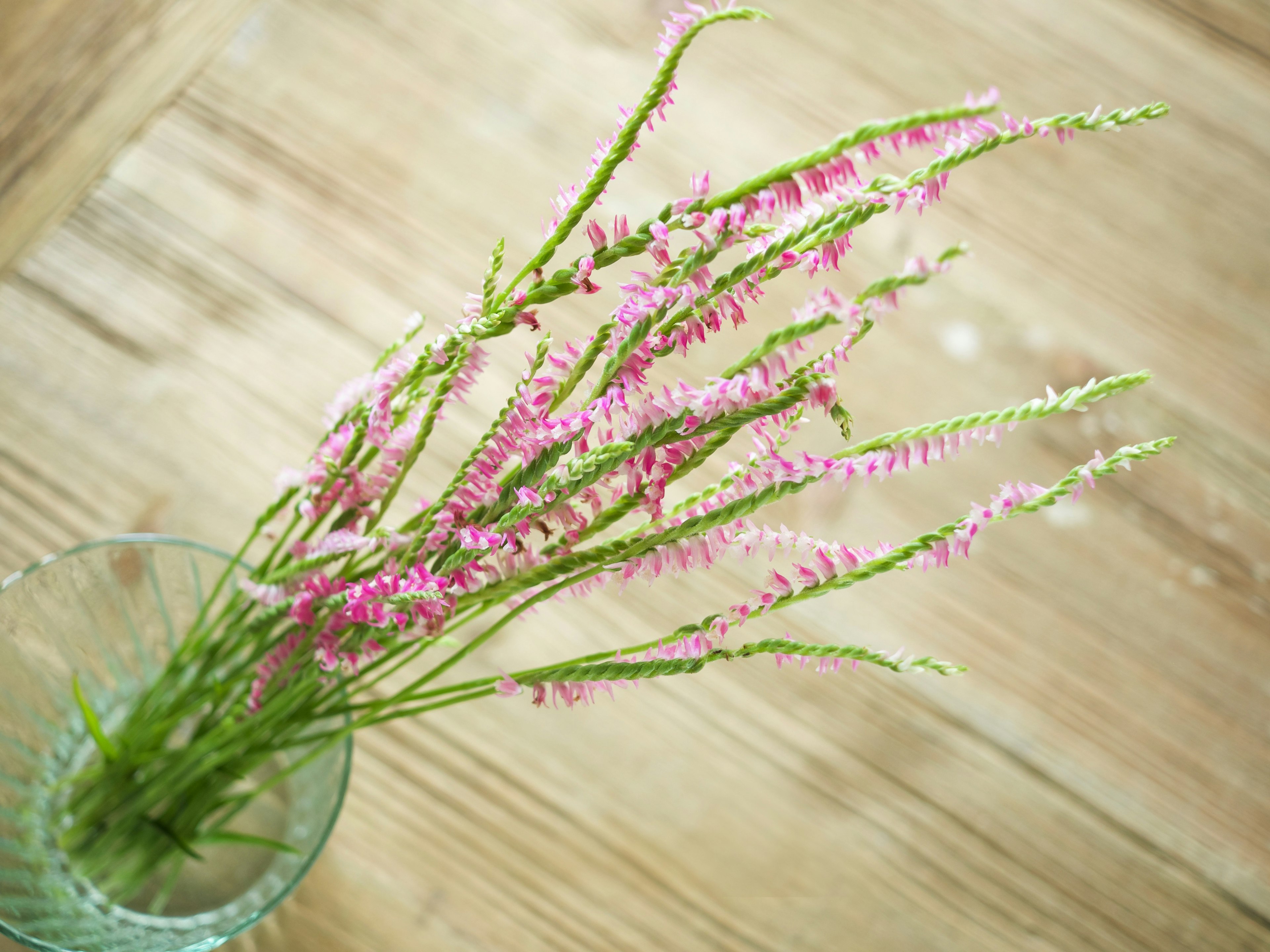 ピンクの花が入った透明な花瓶が木のテーブルの上に置かれている