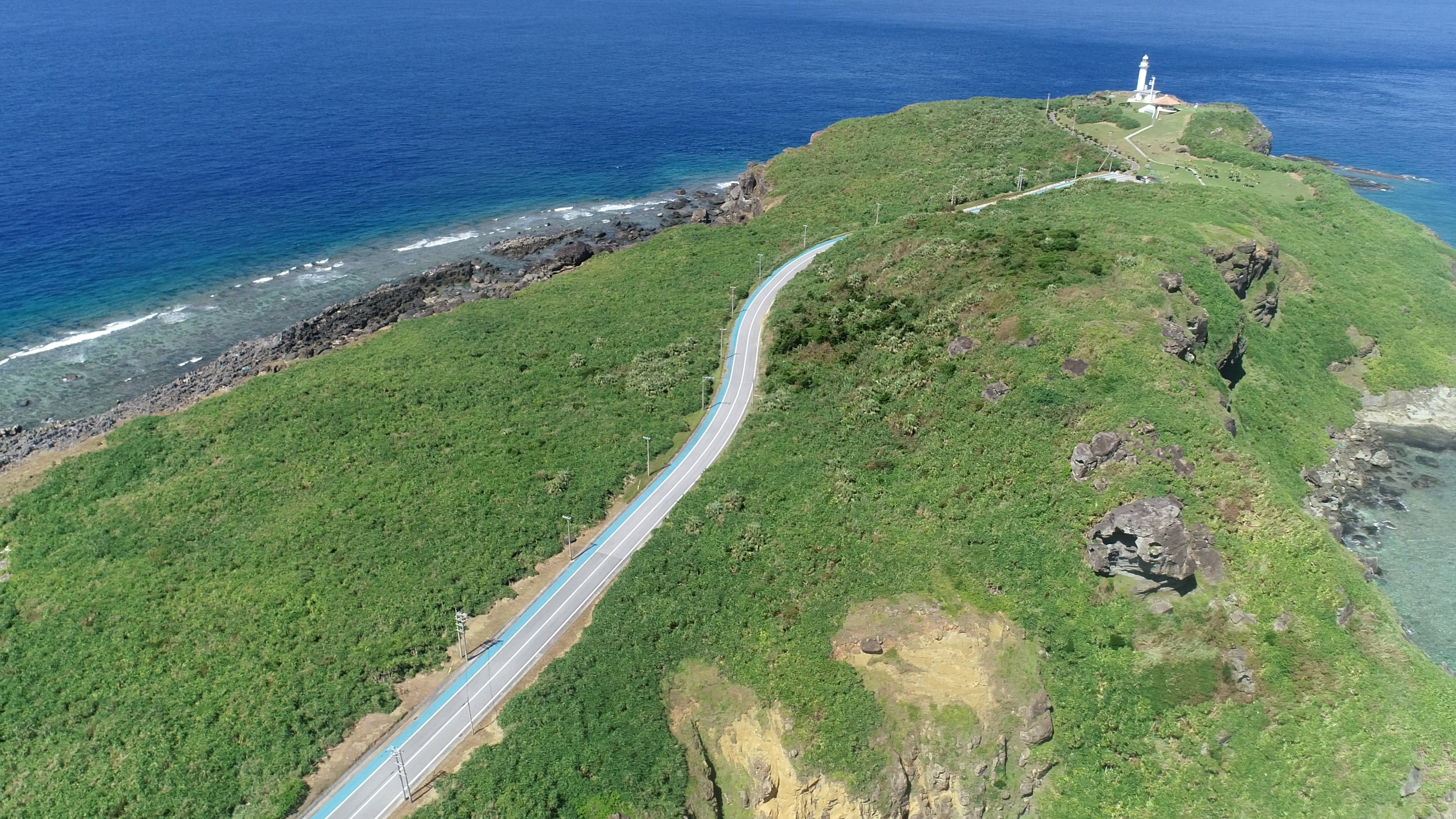 鸟瞰绿色山丘上的弯曲道路和俯瞰蓝色海洋的灯塔