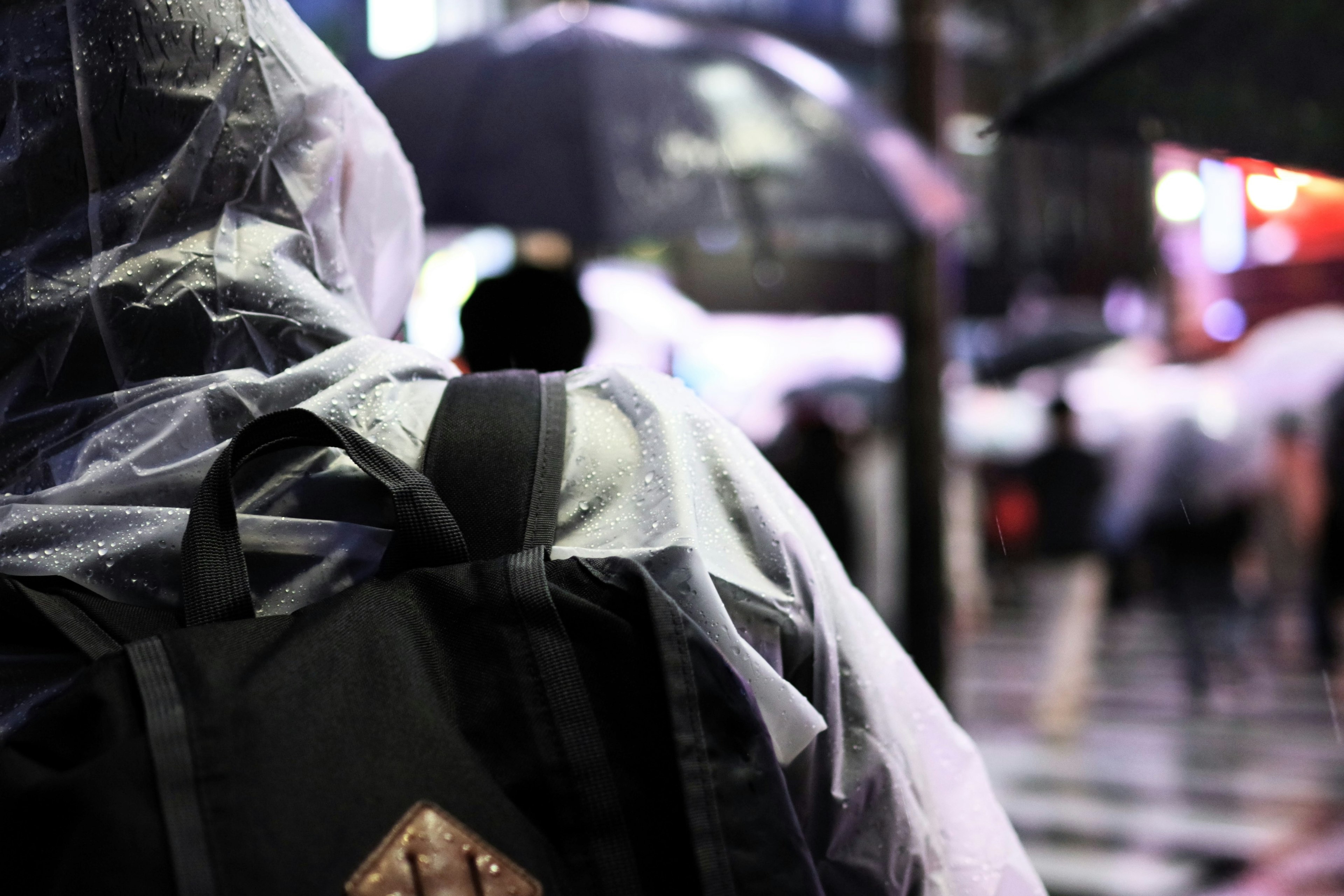 Person wearing a transparent raincoat in the rain with umbrellas in the background