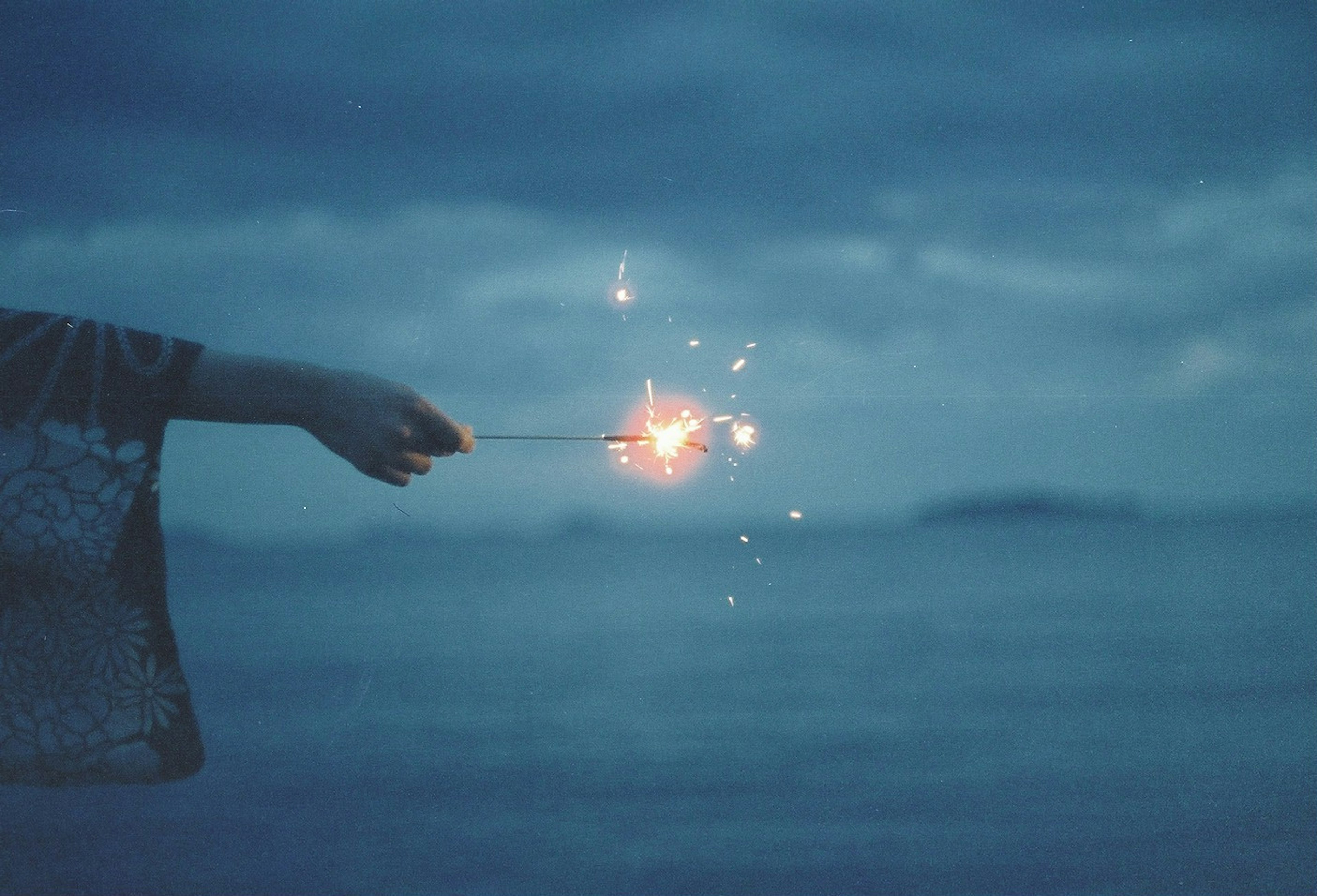 Hand holding a sparkler against a blue ocean backdrop