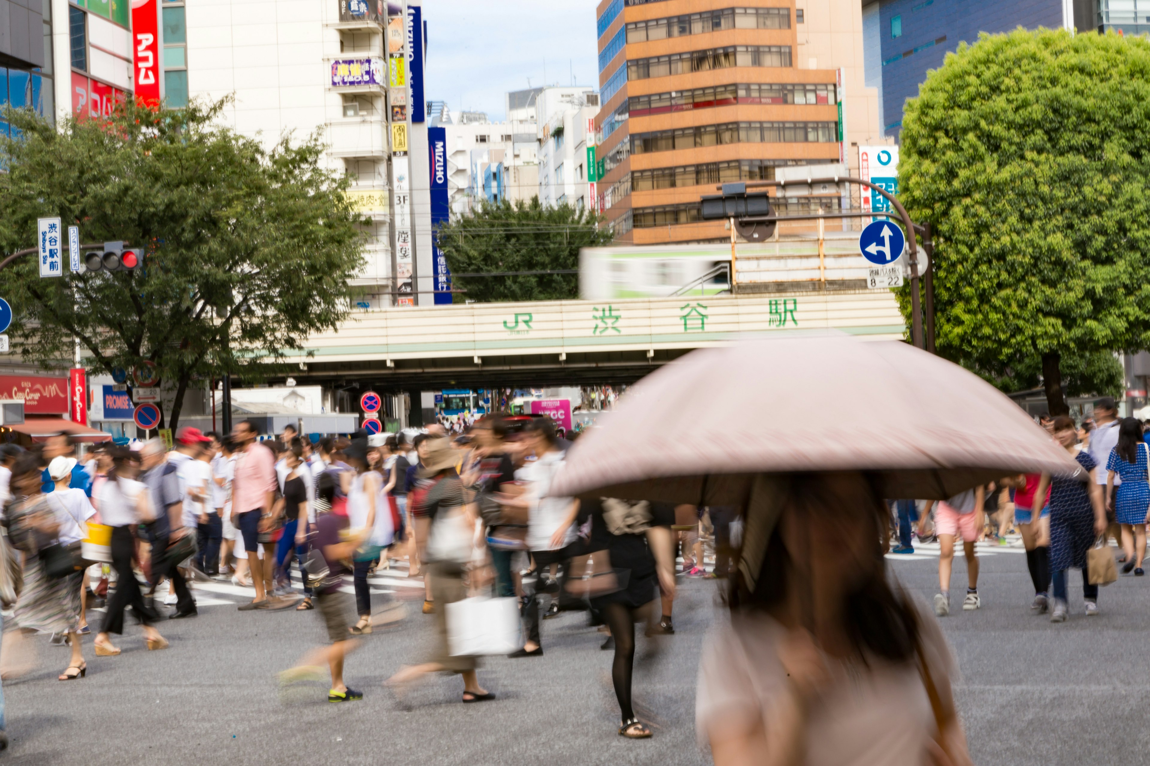 Belebte Kreuzung in Tokio mit Menschen, die überqueren, und einer Frau mit einem Regenschirm im Vordergrund