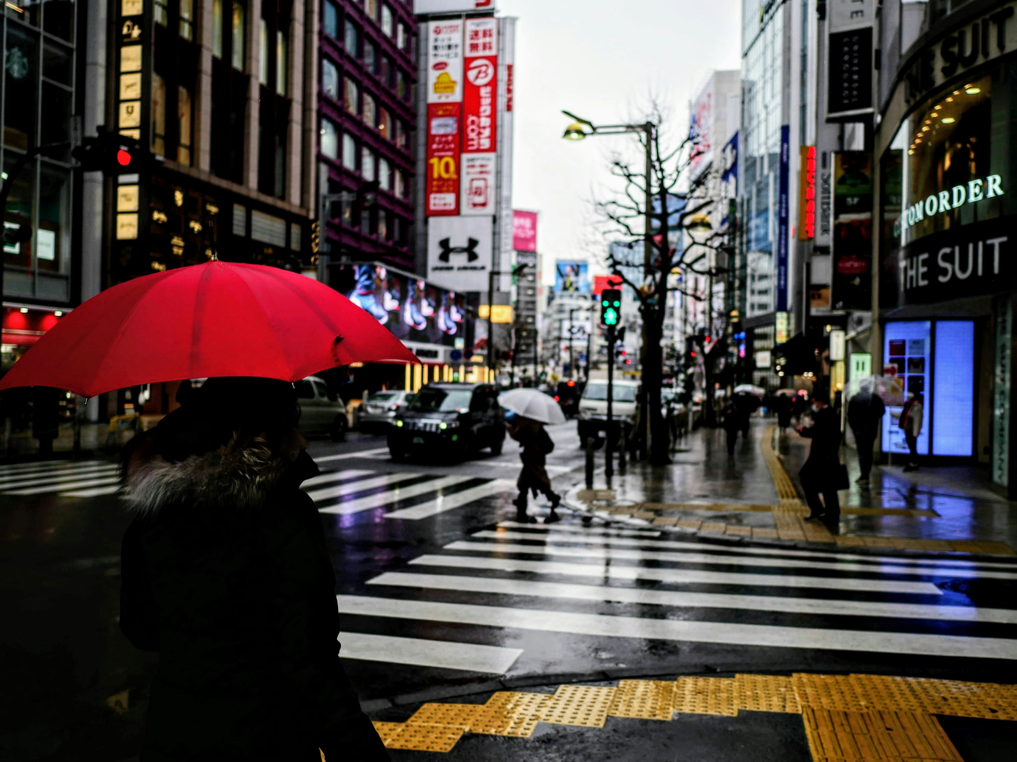 ผู้คนที่มีร่มสีแดงข้ามถนนในสายฝนท่ามกลางตึกสูง