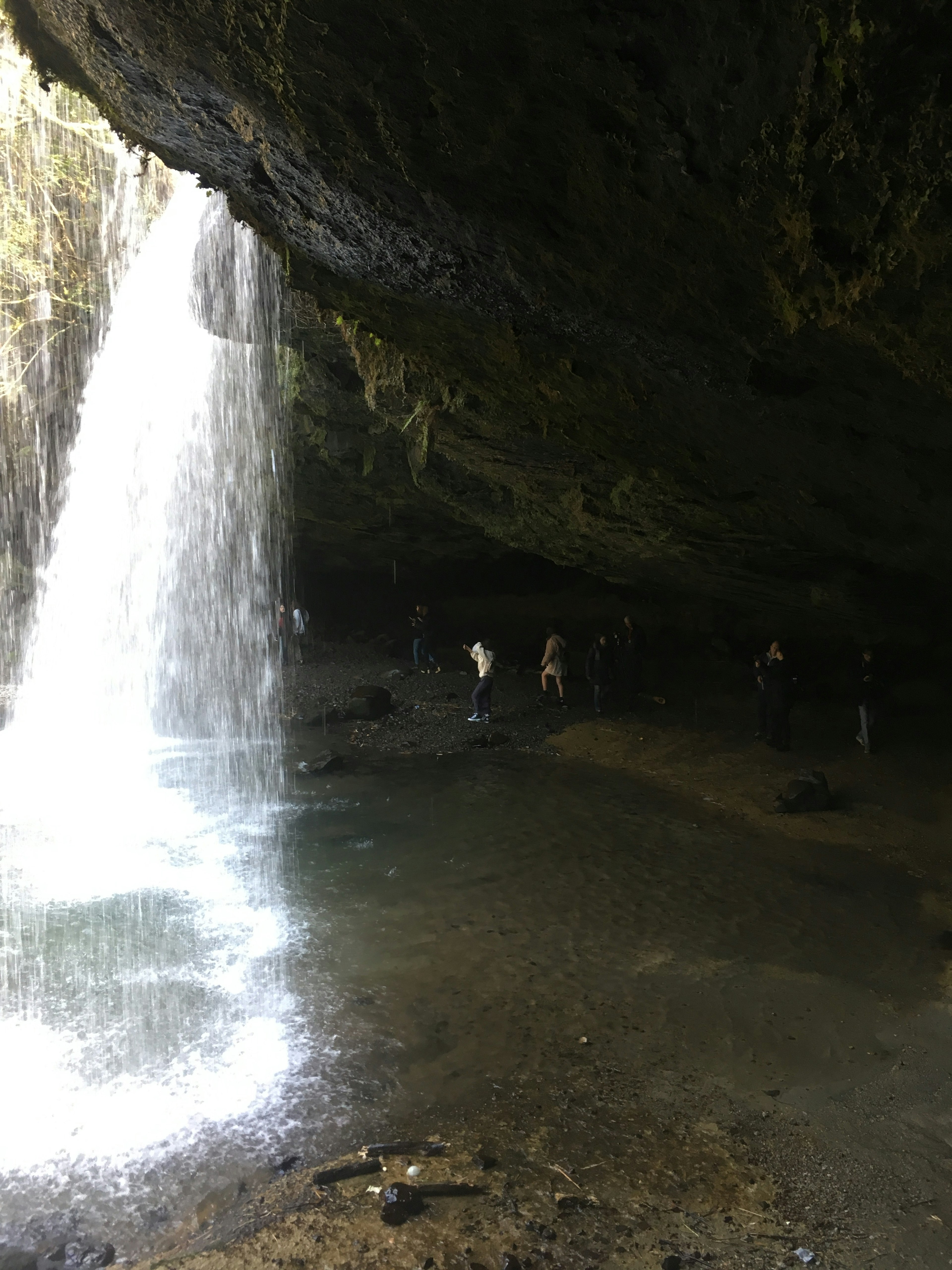 People exploring the area behind a waterfall inside a dark cave