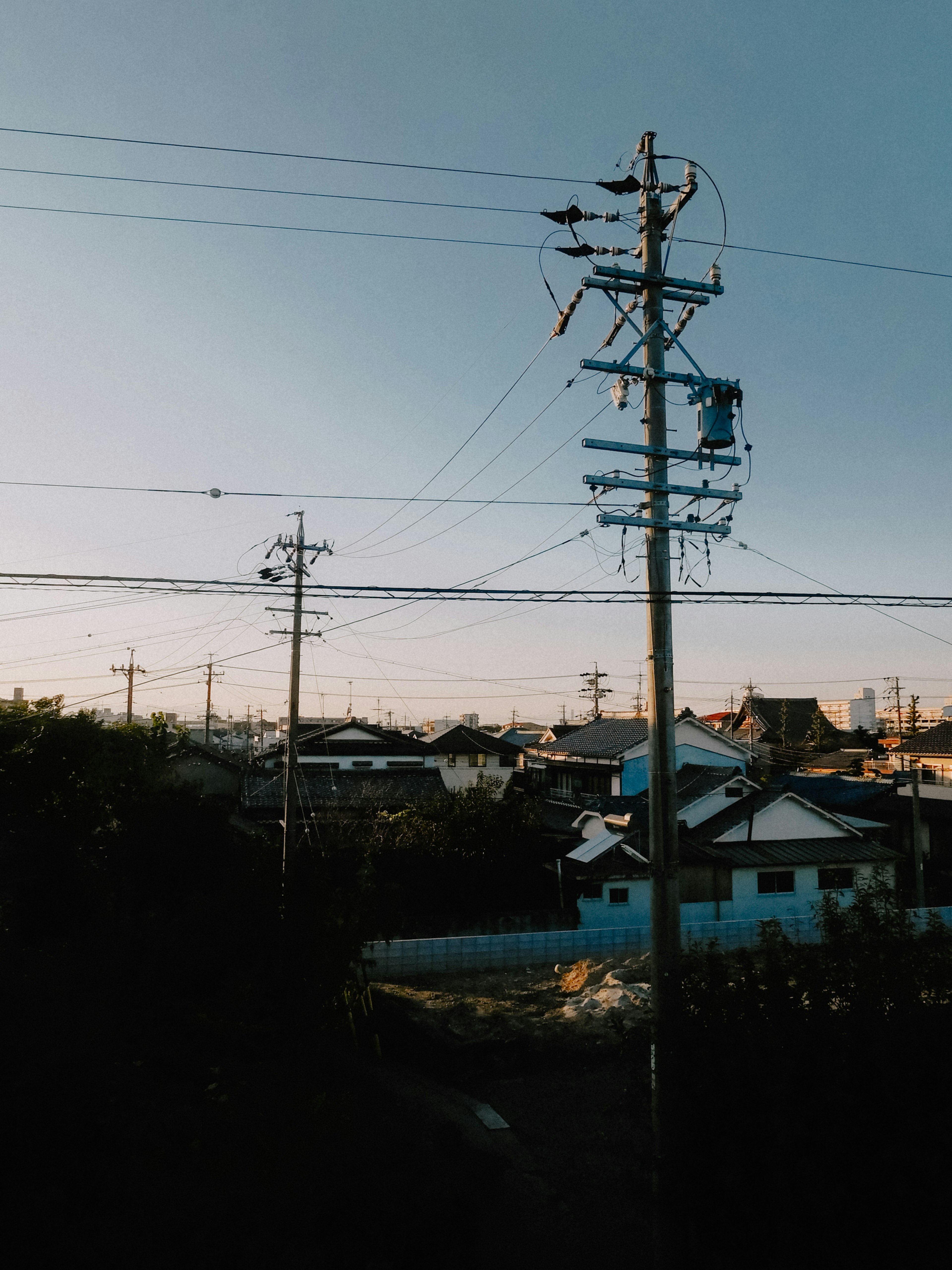 Líneas eléctricas y casas al atardecer con cielo azul claro