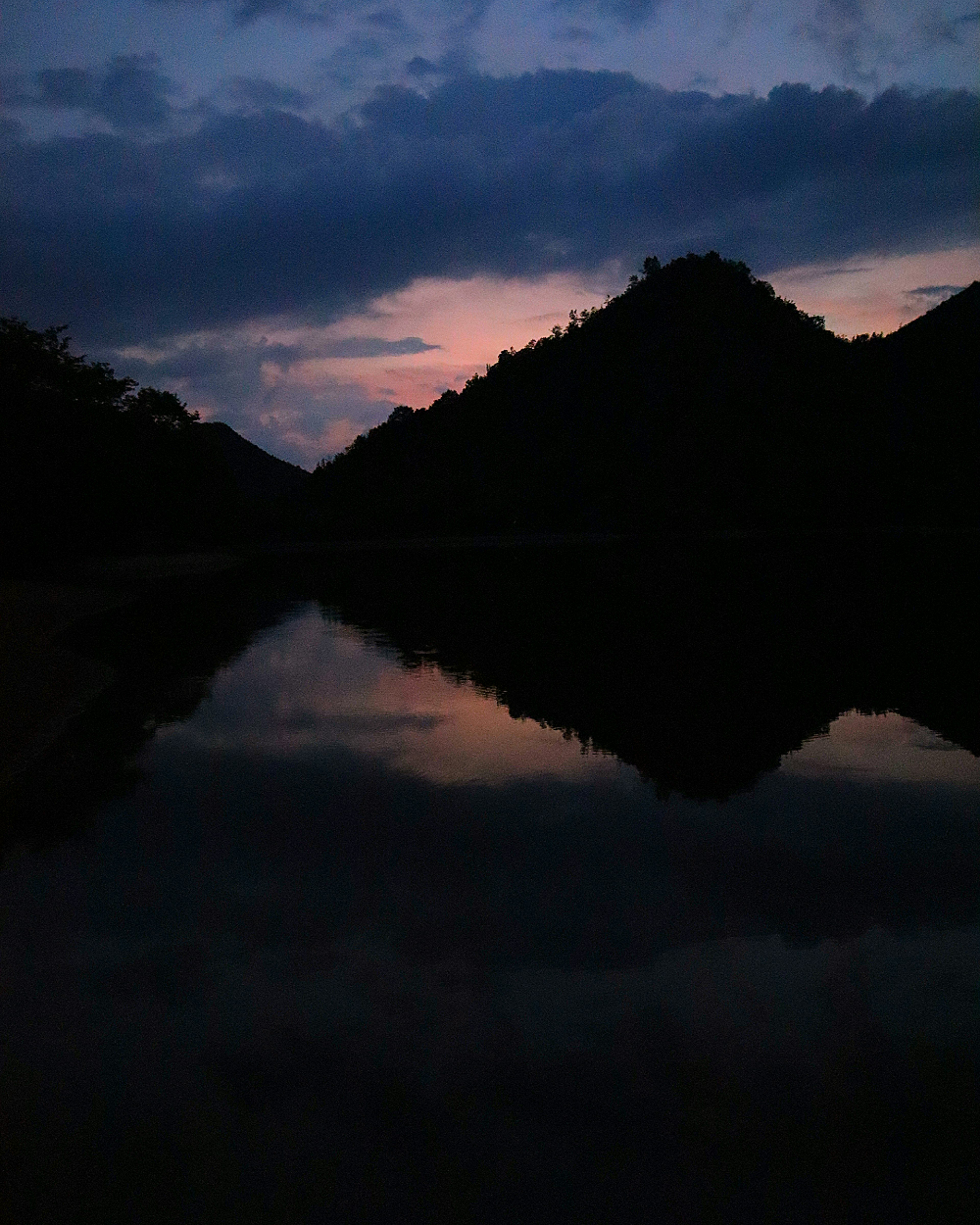 Pemandangan indah pegunungan yang memantul di air tenang saat matahari terbenam