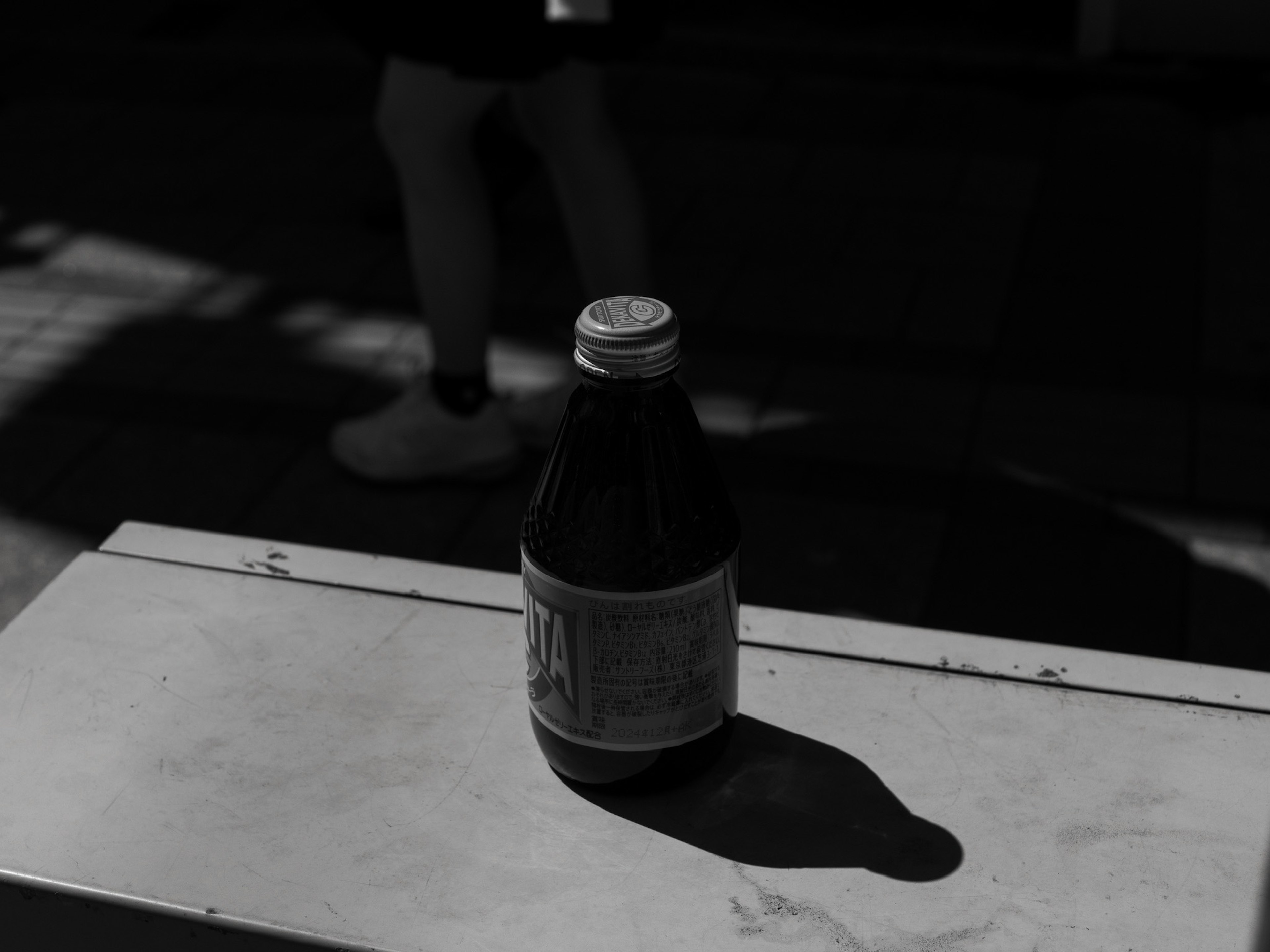 Una botella proyectando una sombra sobre una mesa blanca en un entorno monocromático