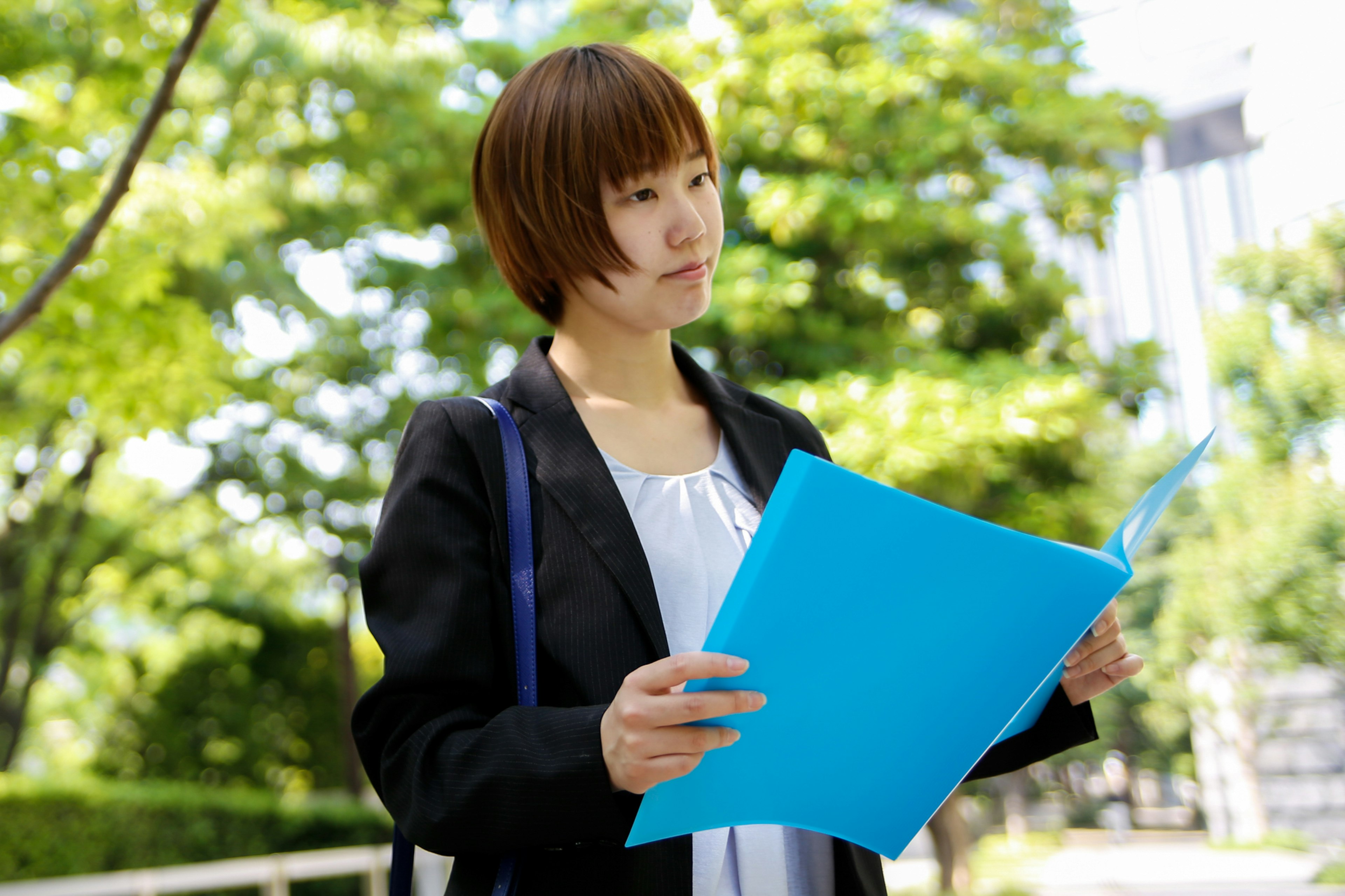 A woman in business attire holding a blue folder standing in a park