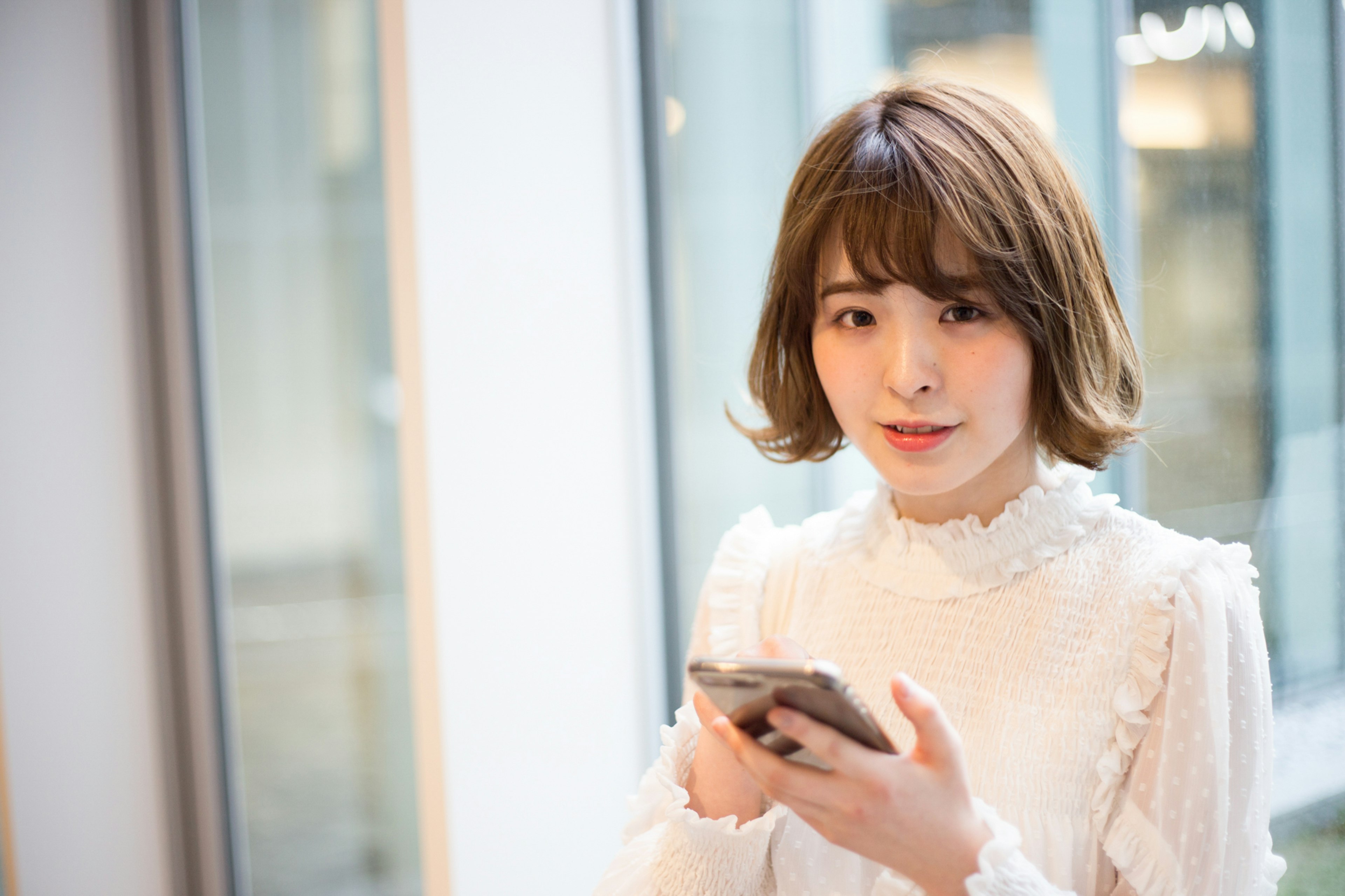 Young woman standing by a window holding a smartphone