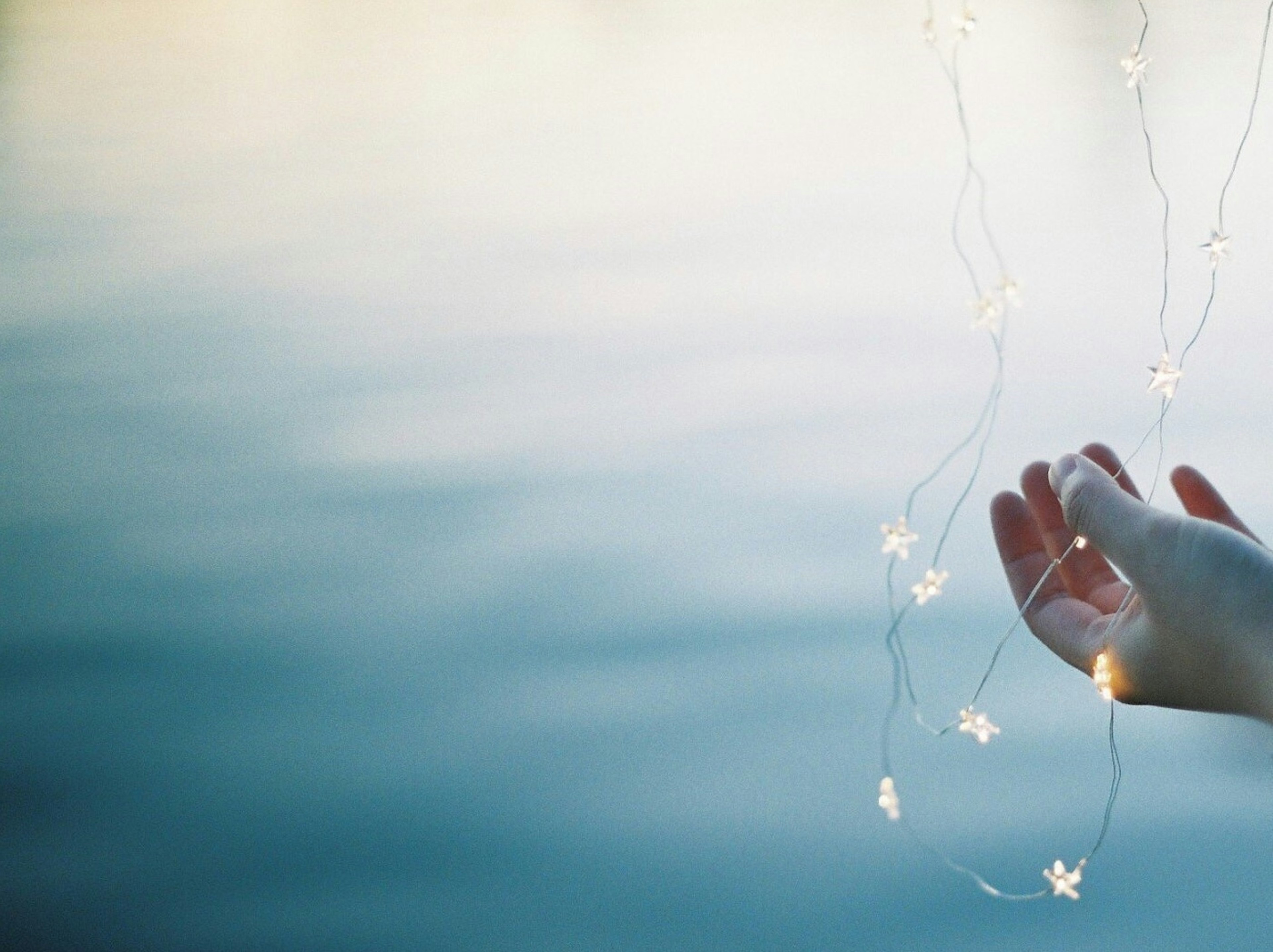 Hand holding star-shaped lights above a reflective water surface