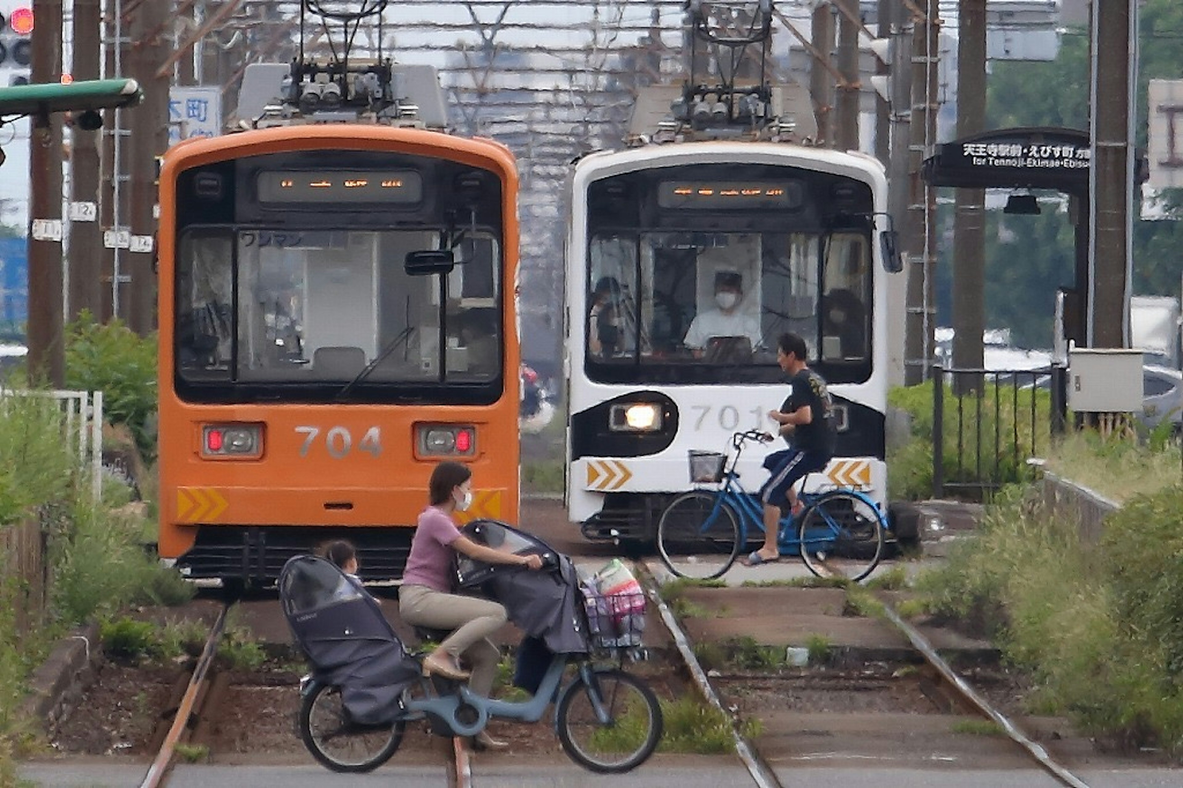 Bicyclist crossing railway tracks with orange and white trains approaching