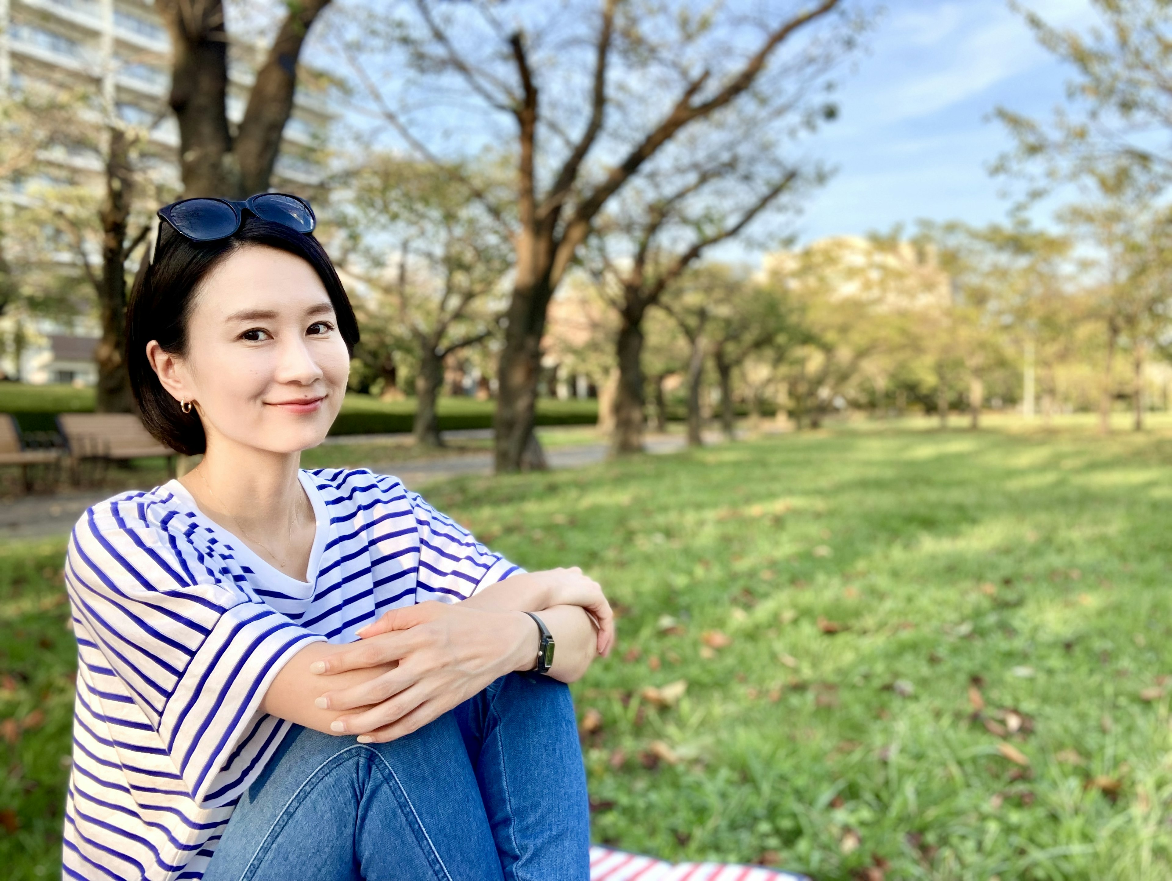 Retrato de una mujer relajándose en un parque con una camisa a rayas y un cielo azul y césped verde de fondo