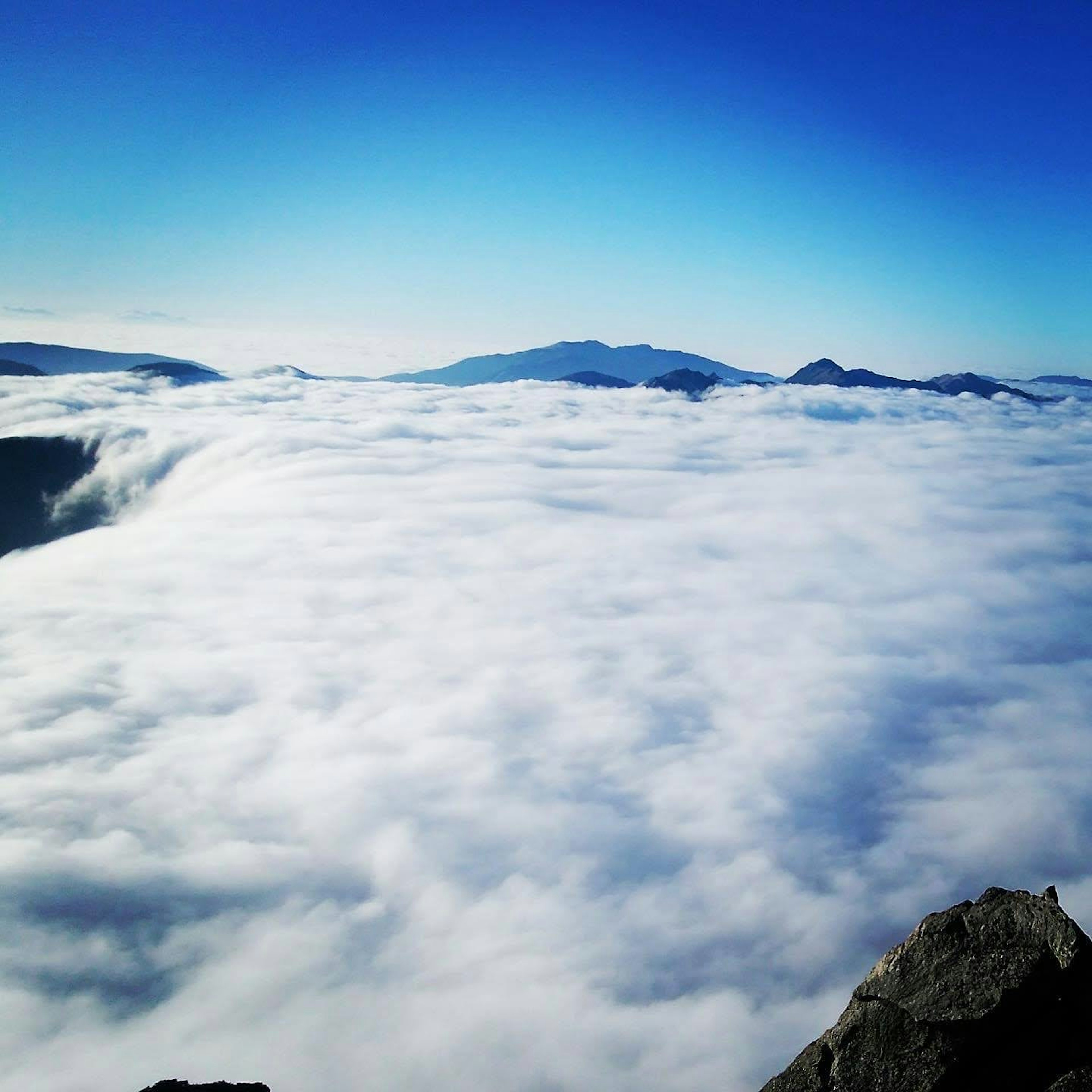 Un mar de nubes con montañas a lo lejos bajo un cielo azul claro