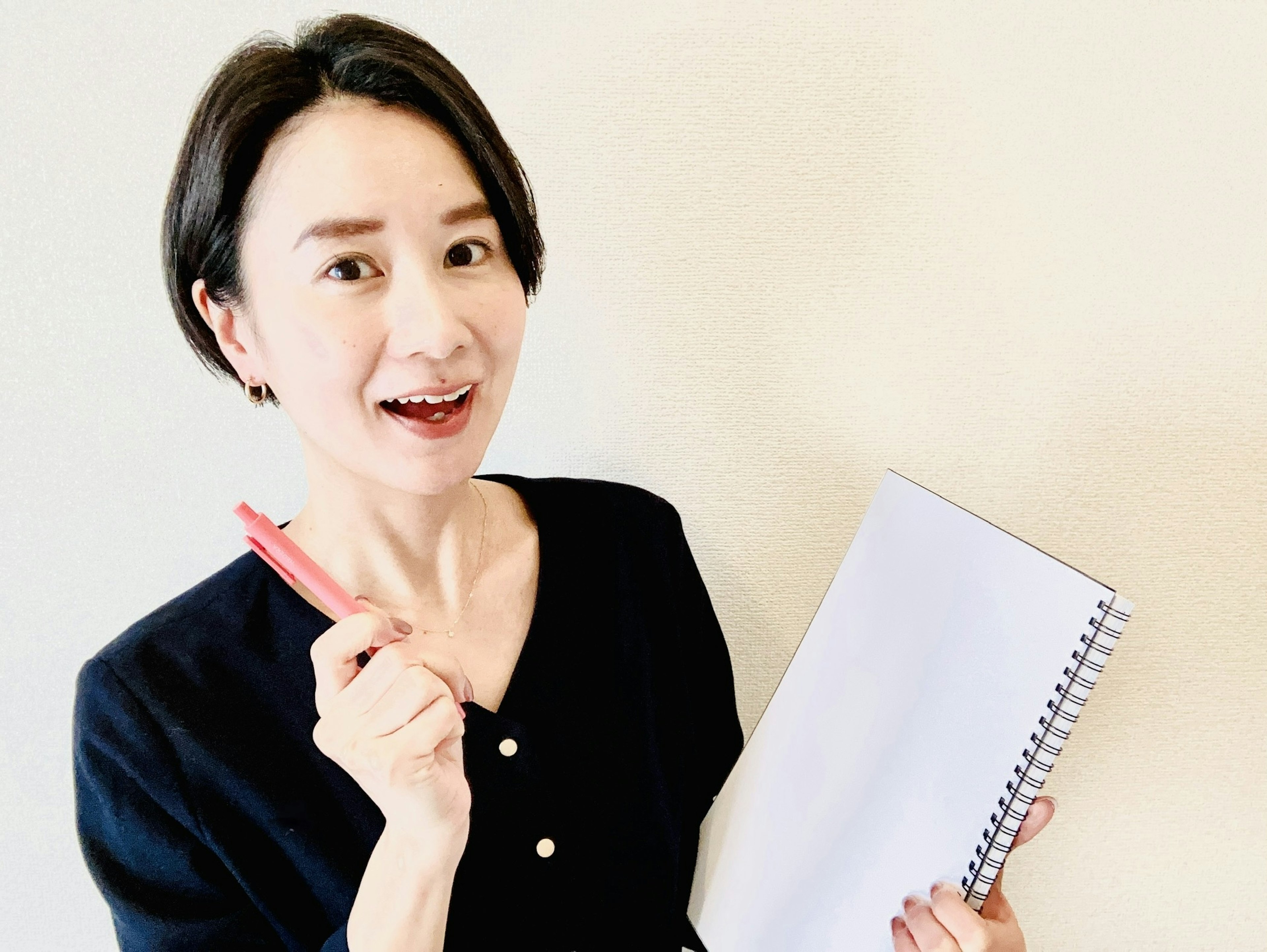 Una mujer sosteniendo un cuaderno y un bolígrafo rojo sonriendo para la cámara