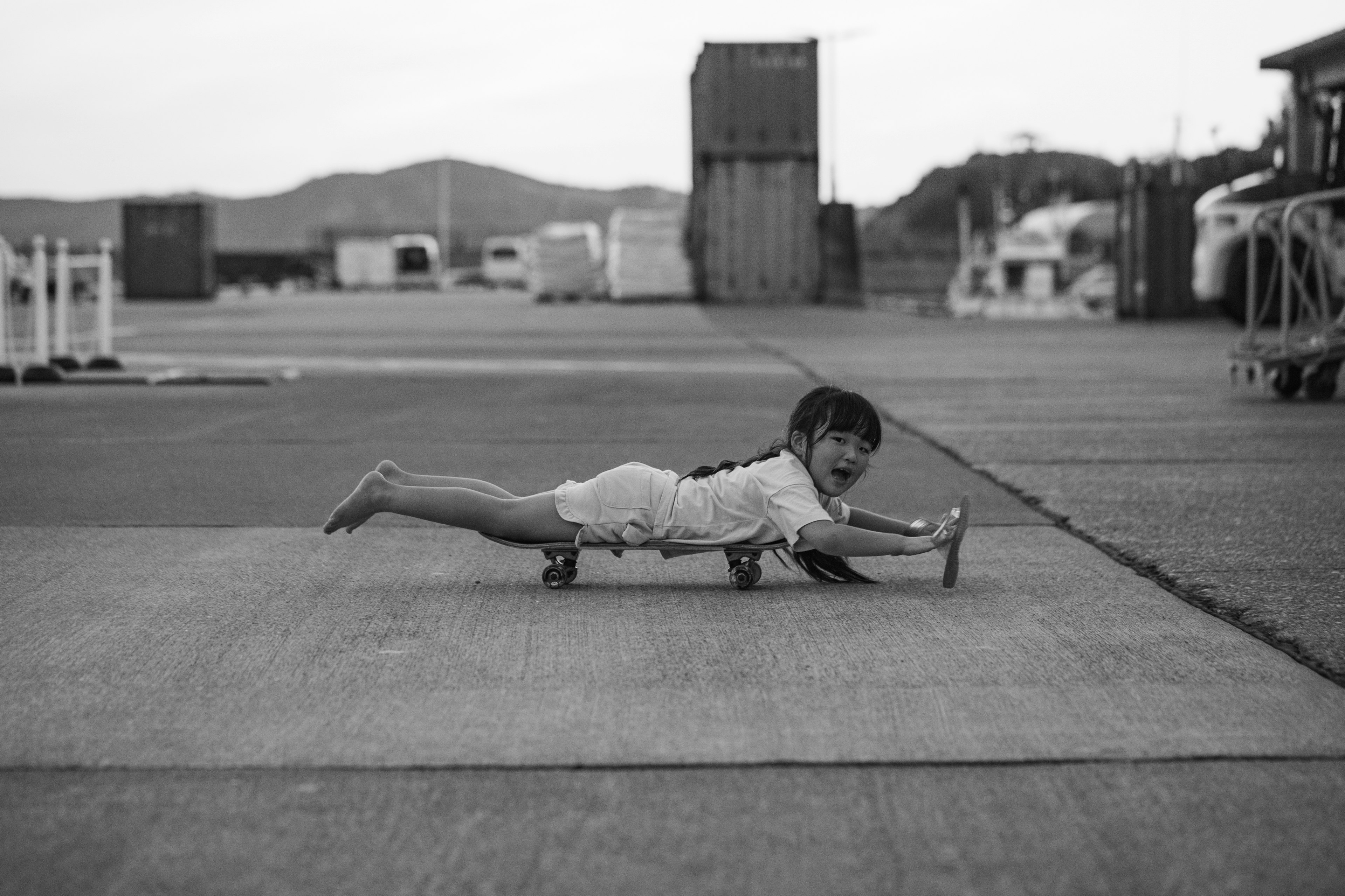 Una niña jugando en el puerto tumbada en el suelo con las manos estiradas hacia adelante en una foto en blanco y negro