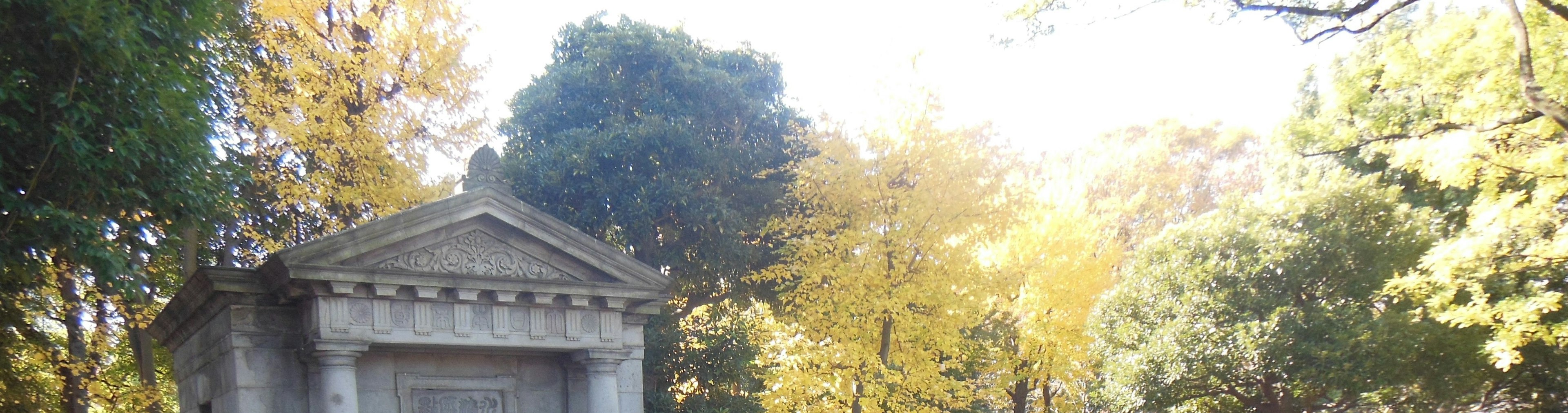 Ein klassischer Grabstein umgeben von grünen Bäumen und herbstlichem Laub