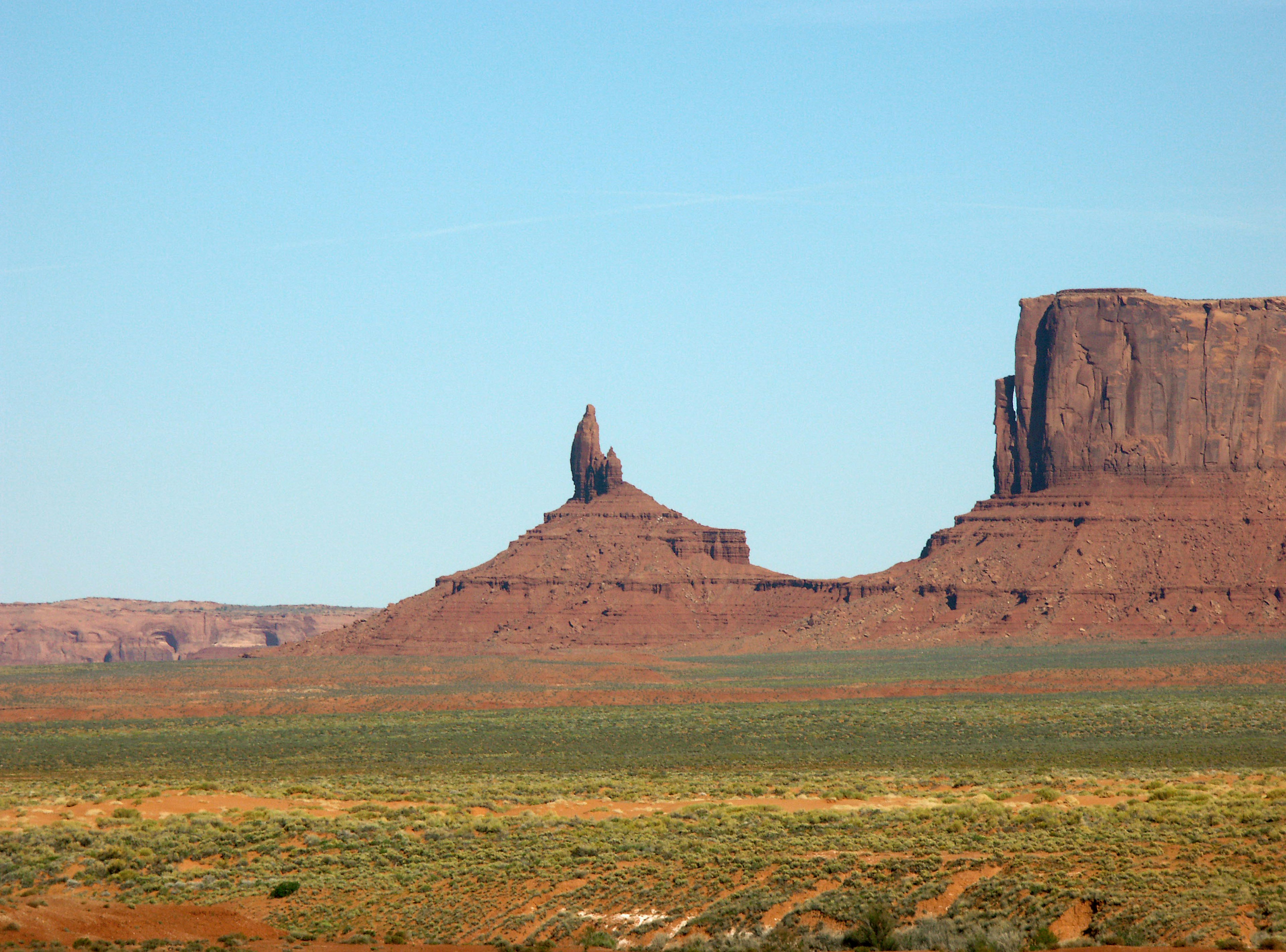 ทิวทัศน์ของ Monument Valley ที่มีรูปทรงหินแดงและท้องฟ้าสีฟ้าใส