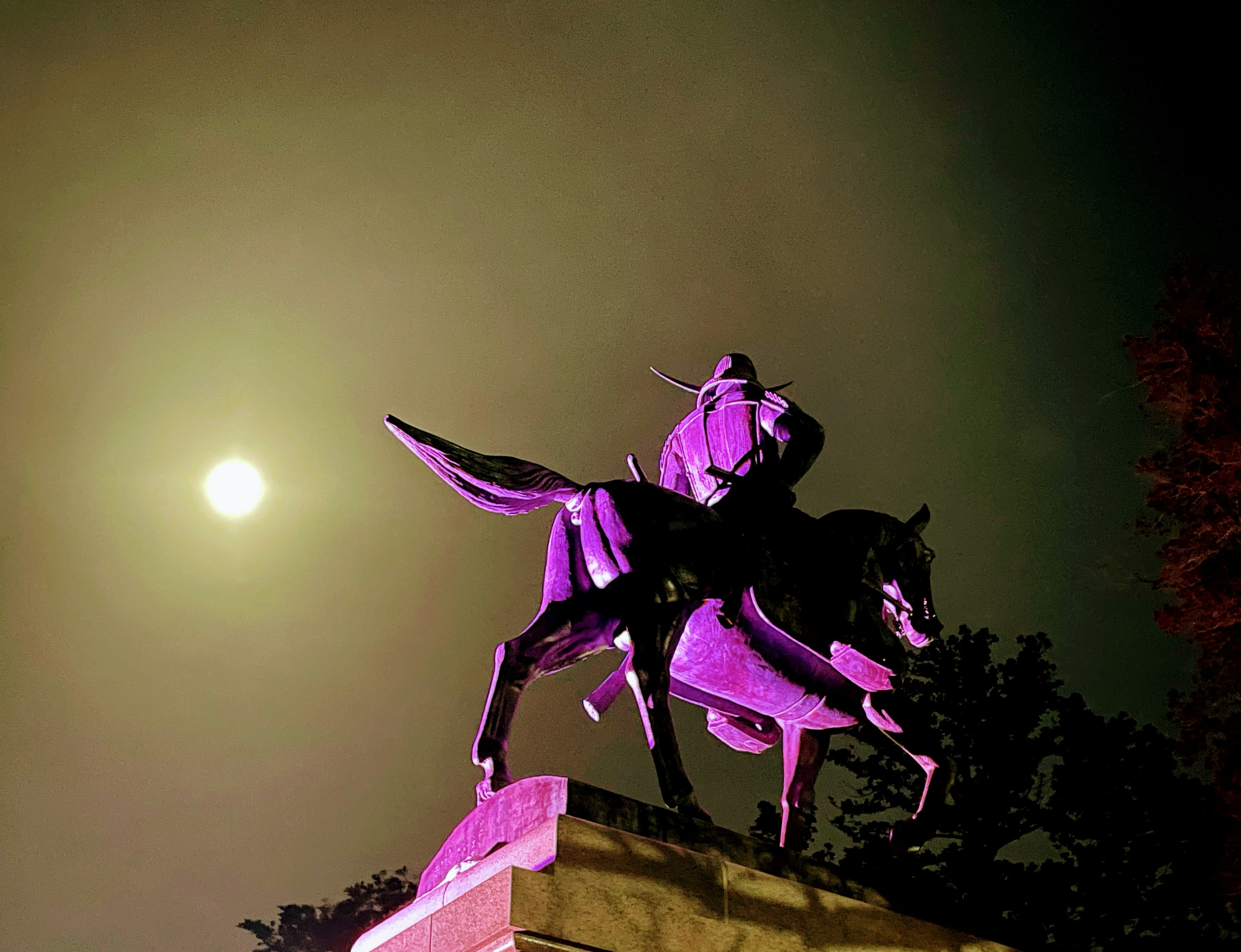 A horse statue illuminated in purple with a full moon in the night sky