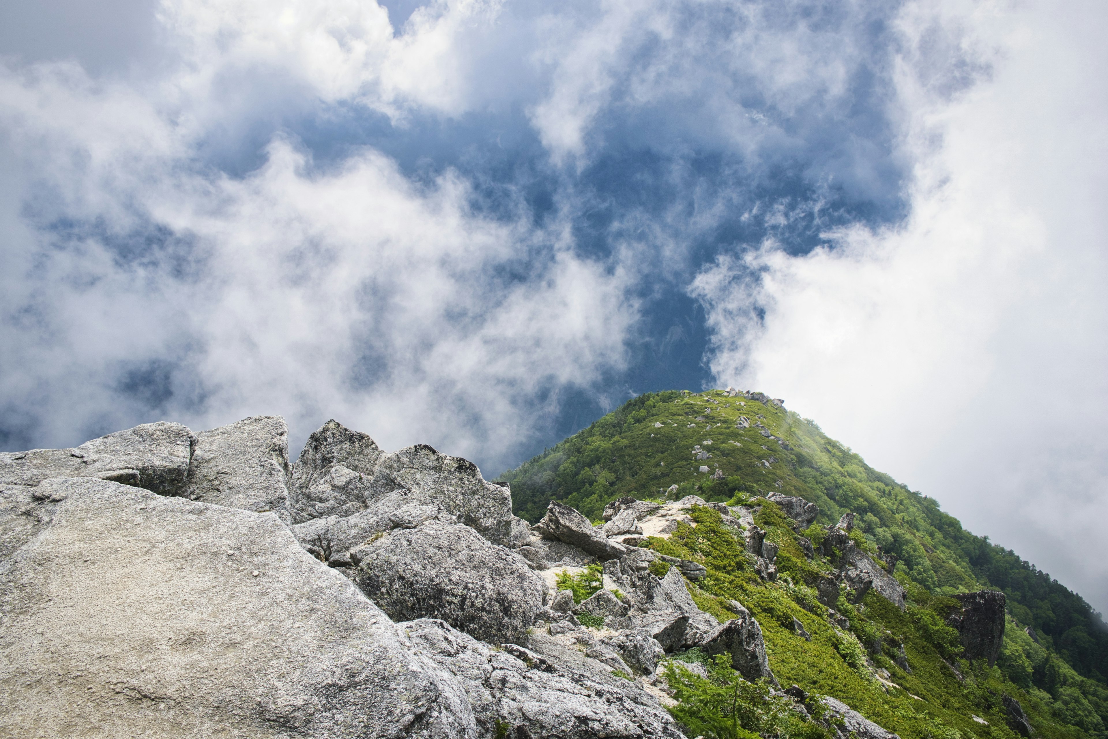 View from mountain peak showing green hill and cloudy blue sky