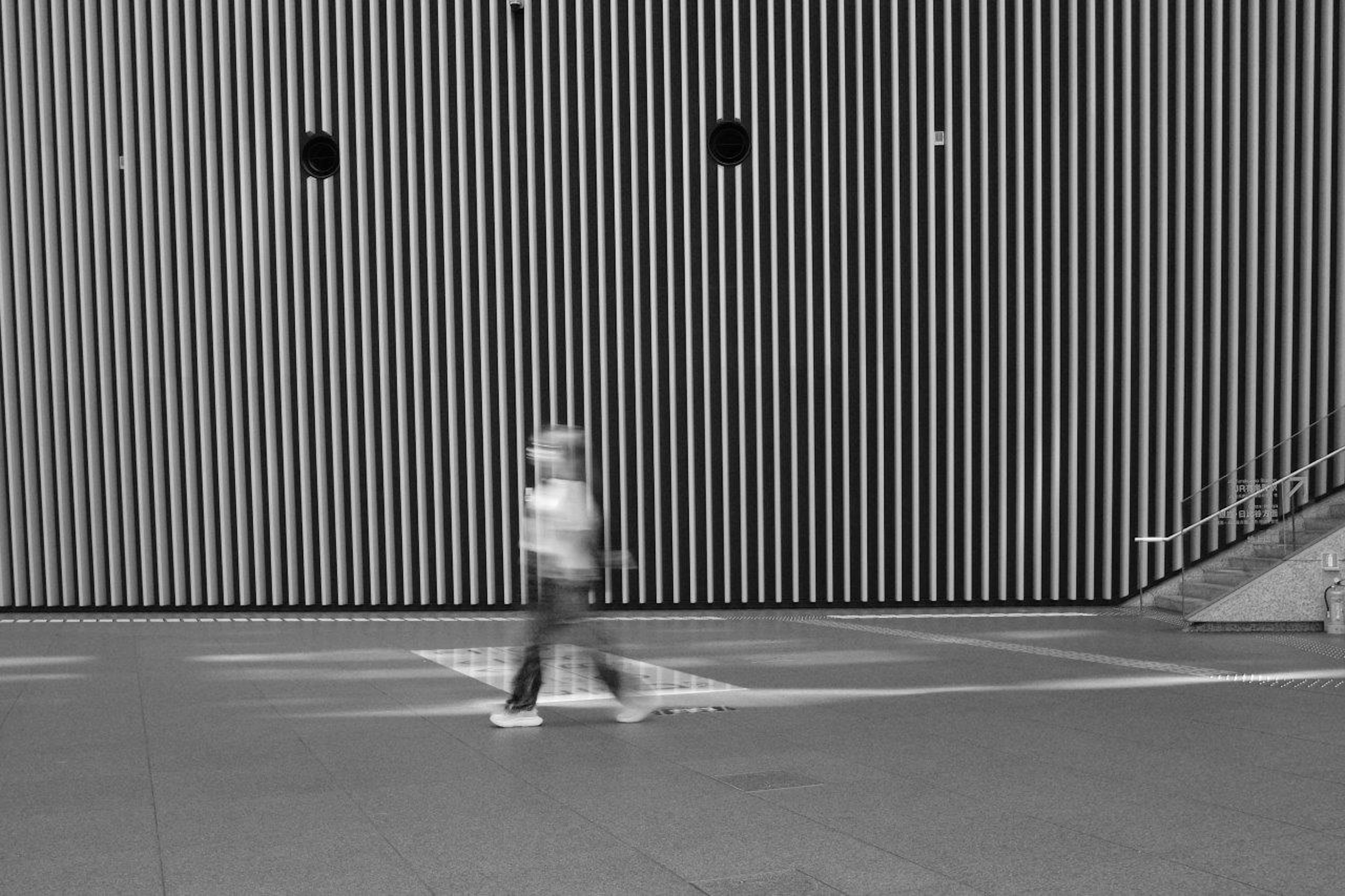 Una persona caminando frente a una pared de rayas verticales en blanco y negro