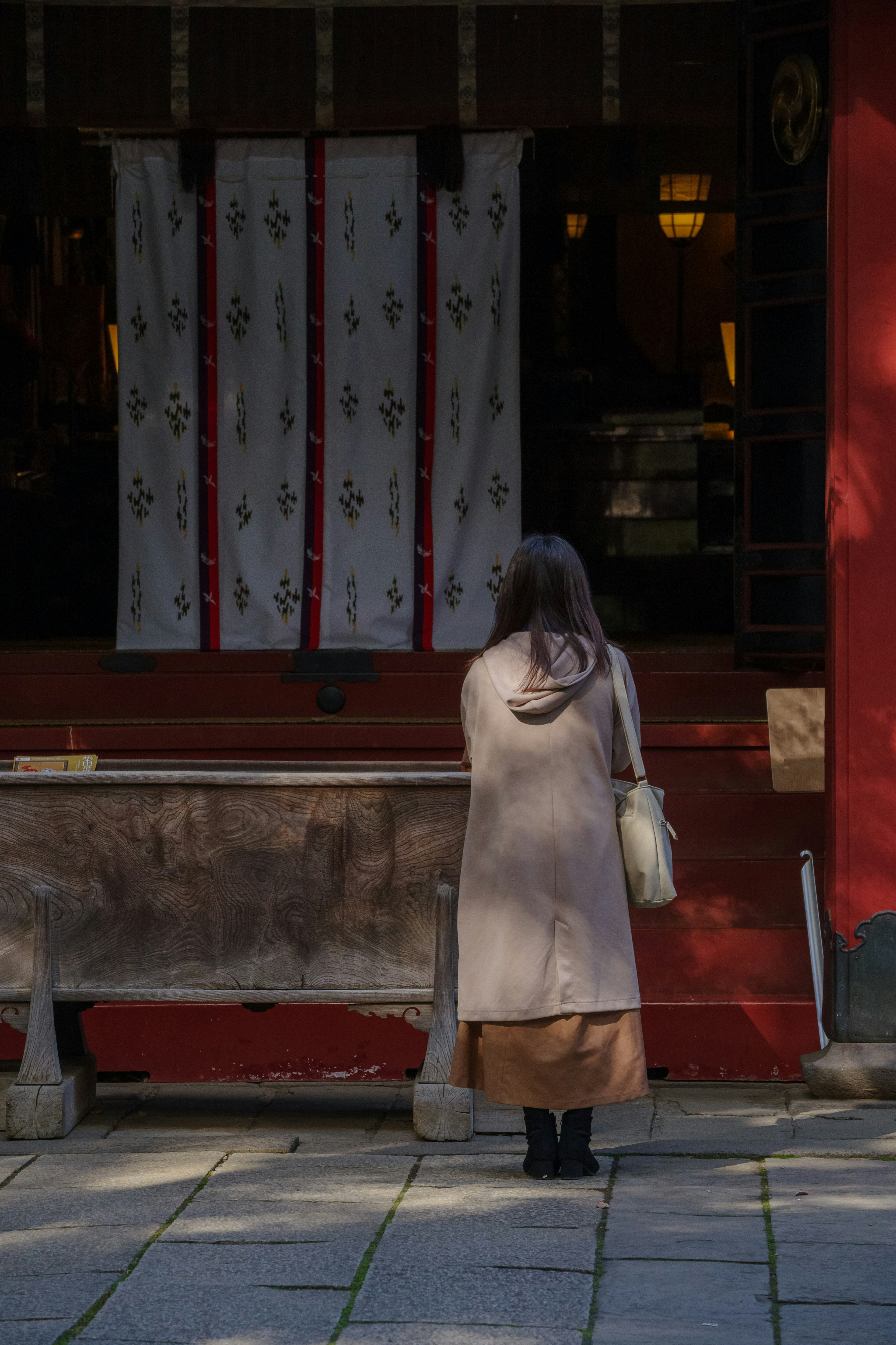 A woman standing in front of a shrine with a red wall and decorative fabric