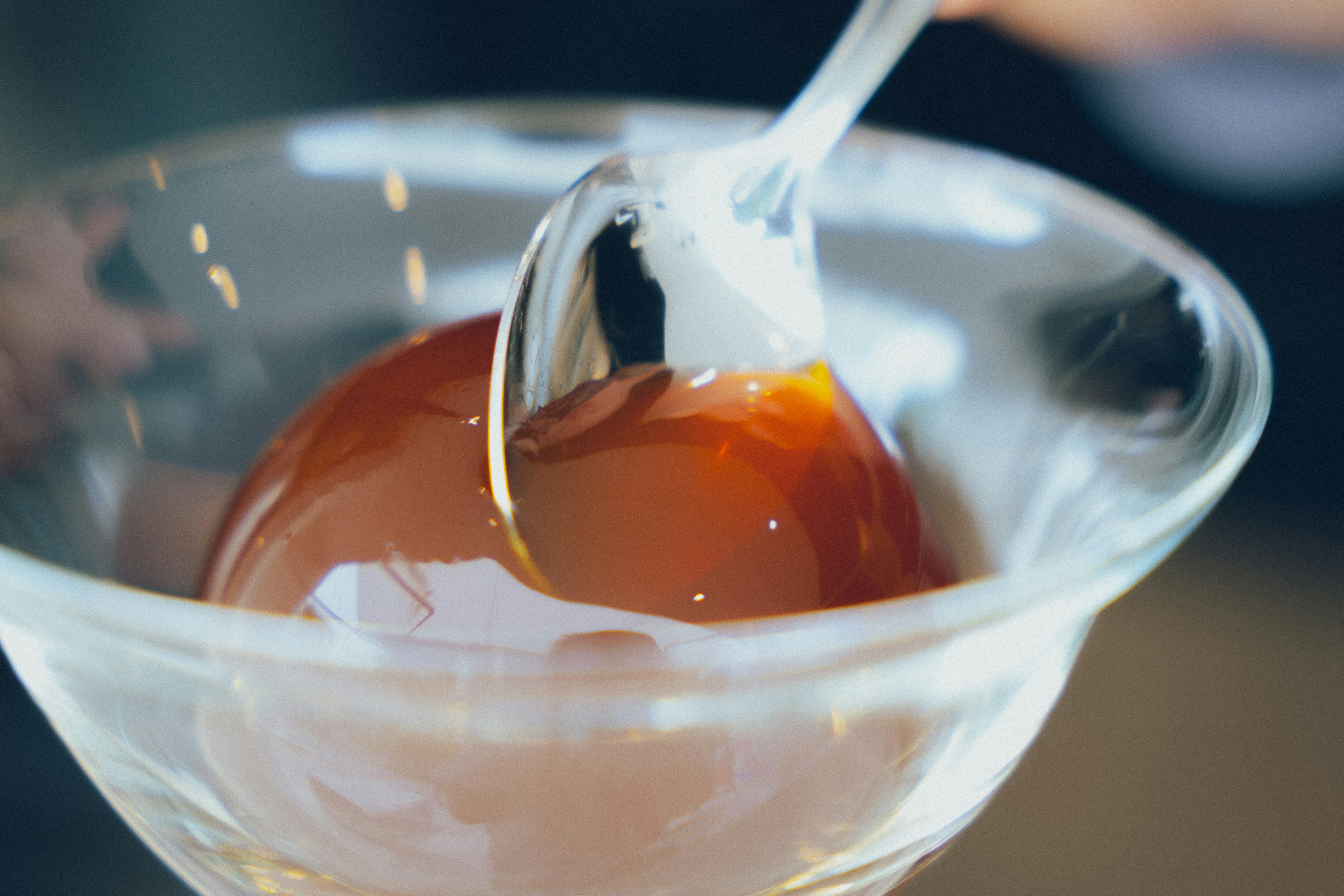 Ein Löffel hebt eine glänzende Dessertkugel in einer klaren Glasschüssel