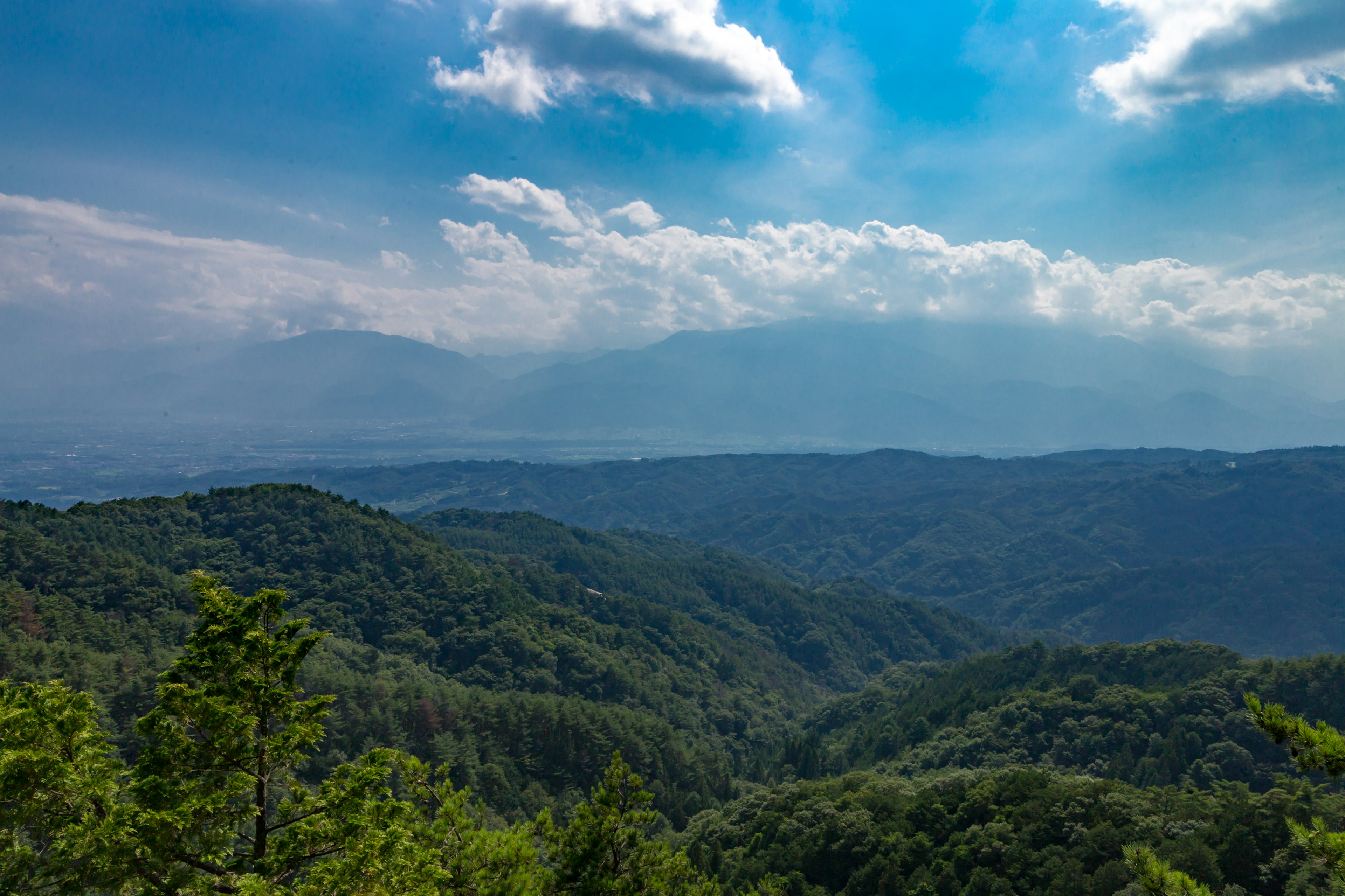 青い空と雲が広がる緑豊かな山々の景色