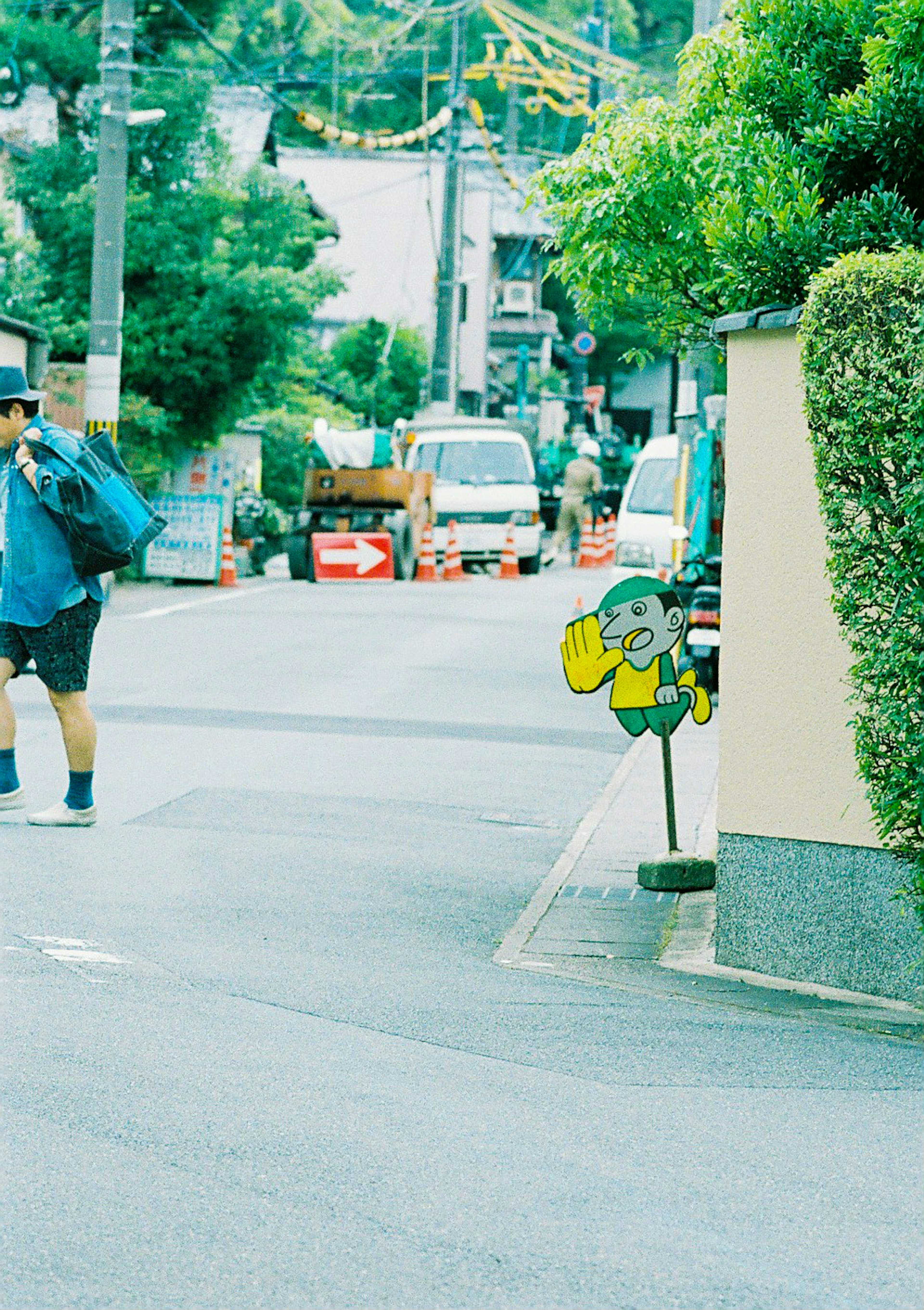 A man in a blue shirt walking on the street with a face-shaped sign visible behind him