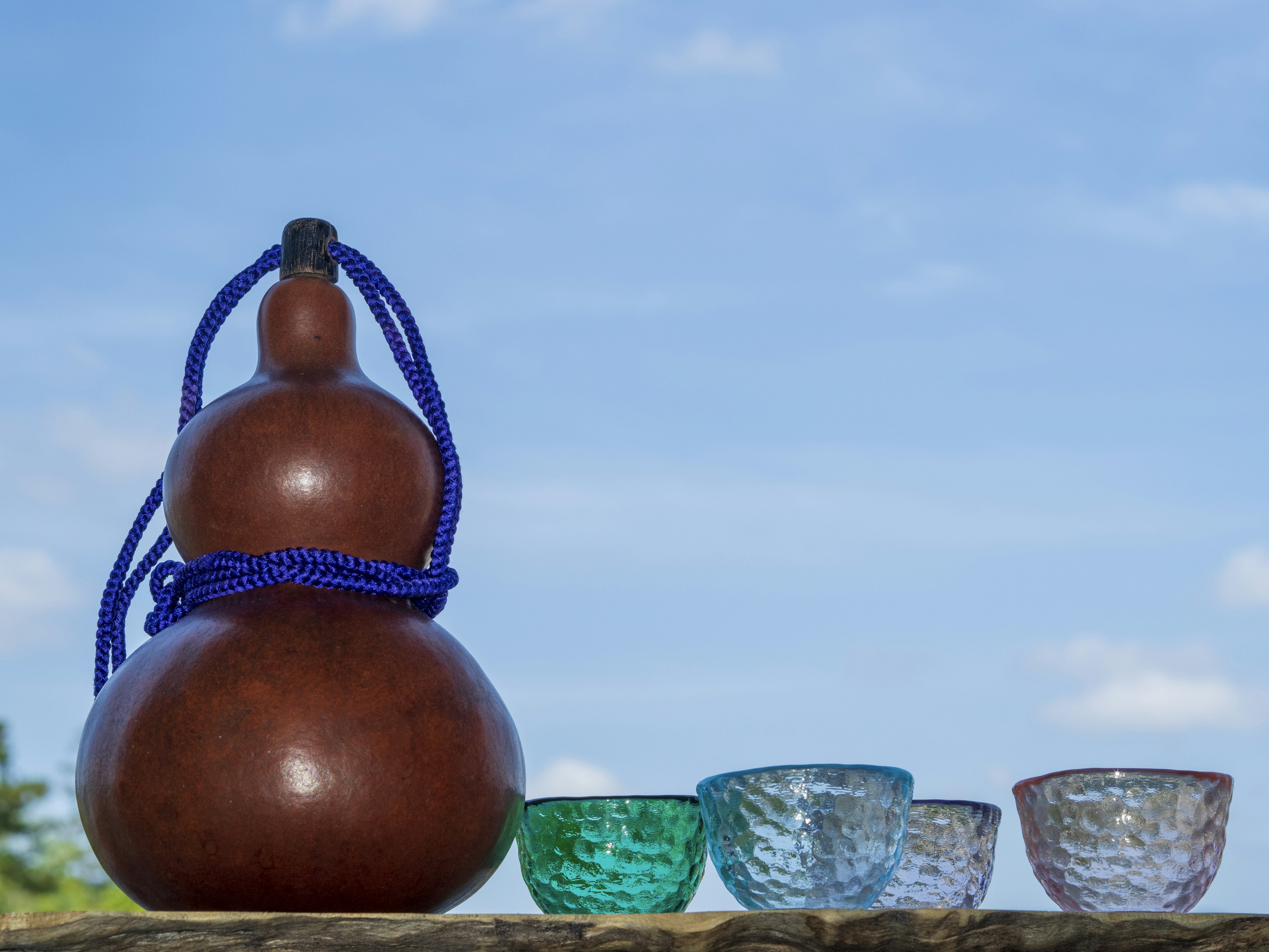 Wooden gourd with a purple rope and colorful glass cups under a blue sky