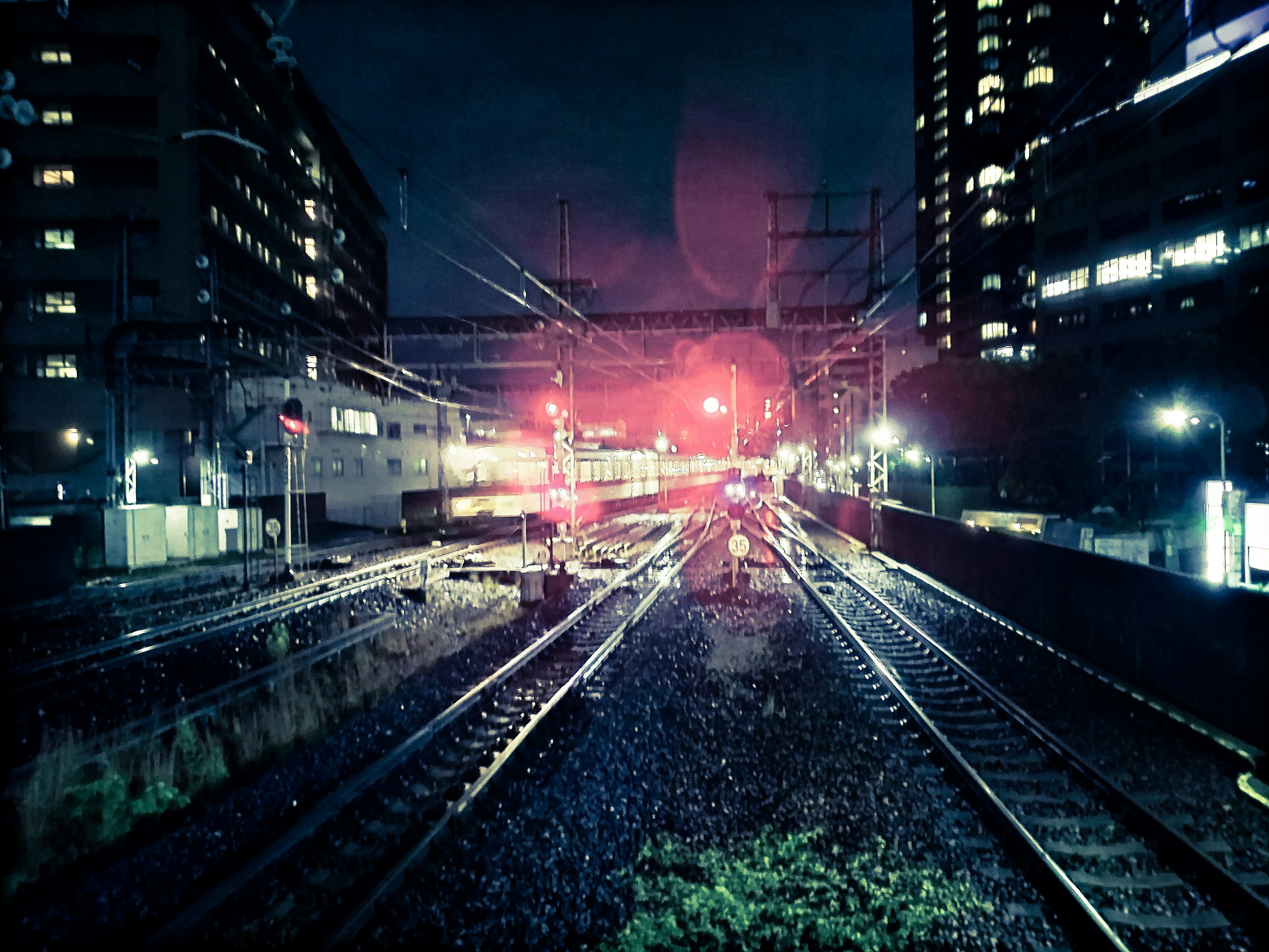 Scène ferroviaire nocturne avec des signaux rouges et des lumières de bâtiments environnants