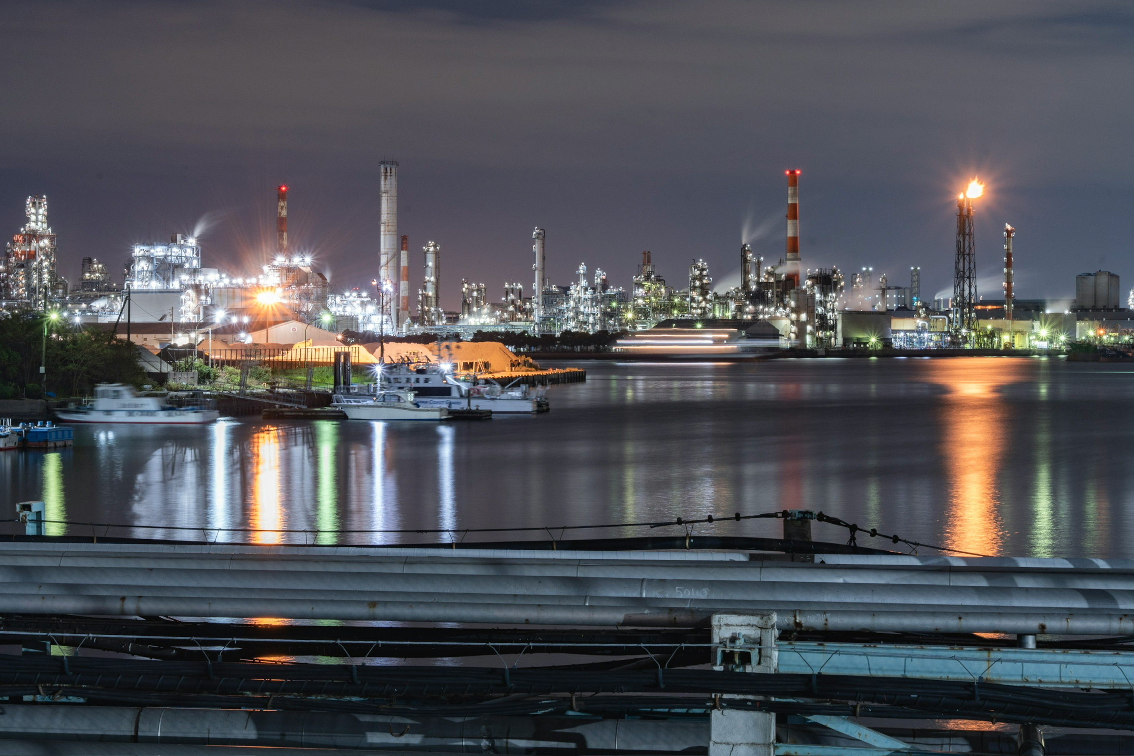 Nachtansicht eines Industriegebiets mit Reflexionen im Wasser und Fabrikschornsteinen