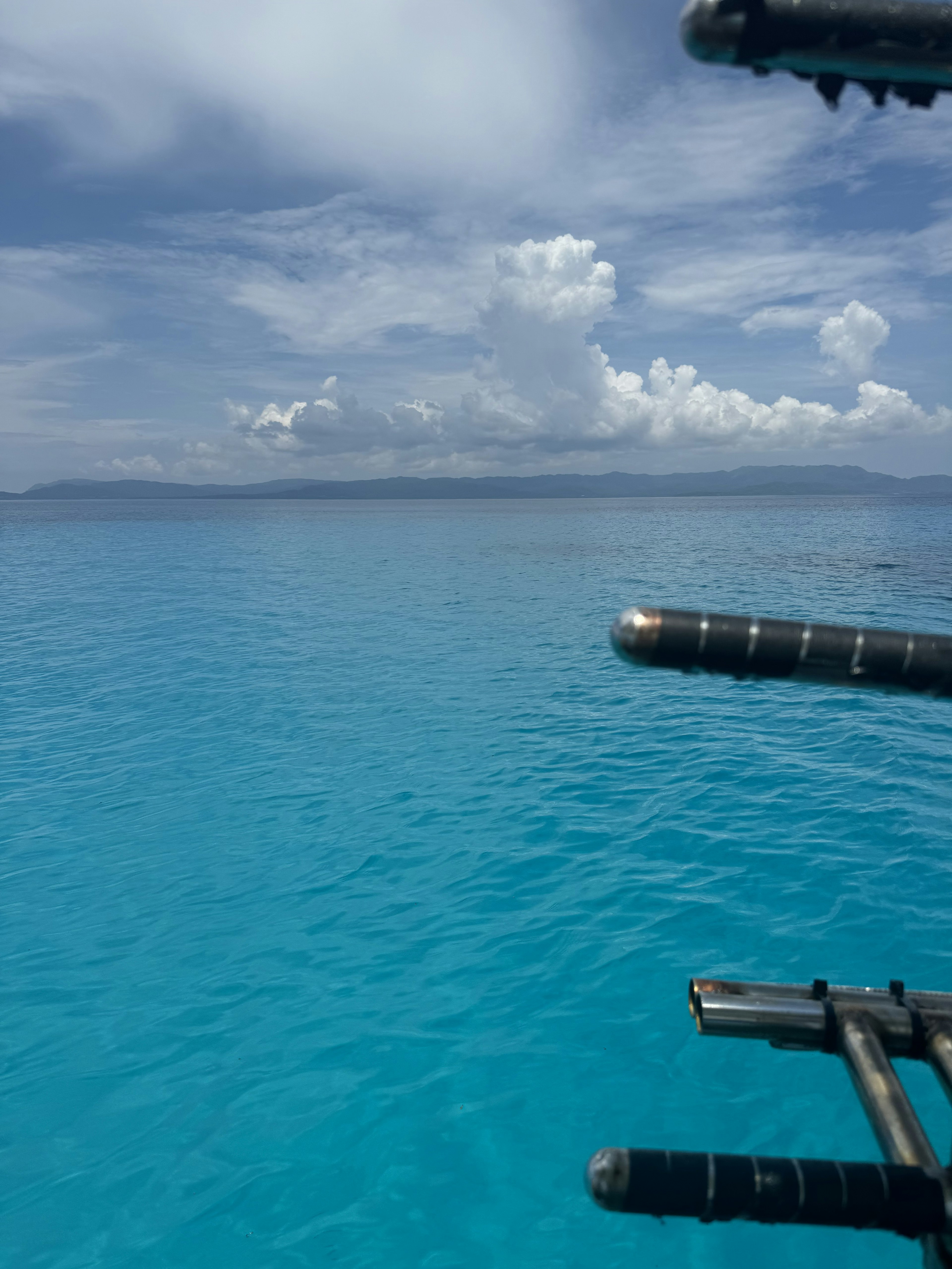 Vibrant turquoise sea with white clouds in the sky part of a boat visible in the foreground