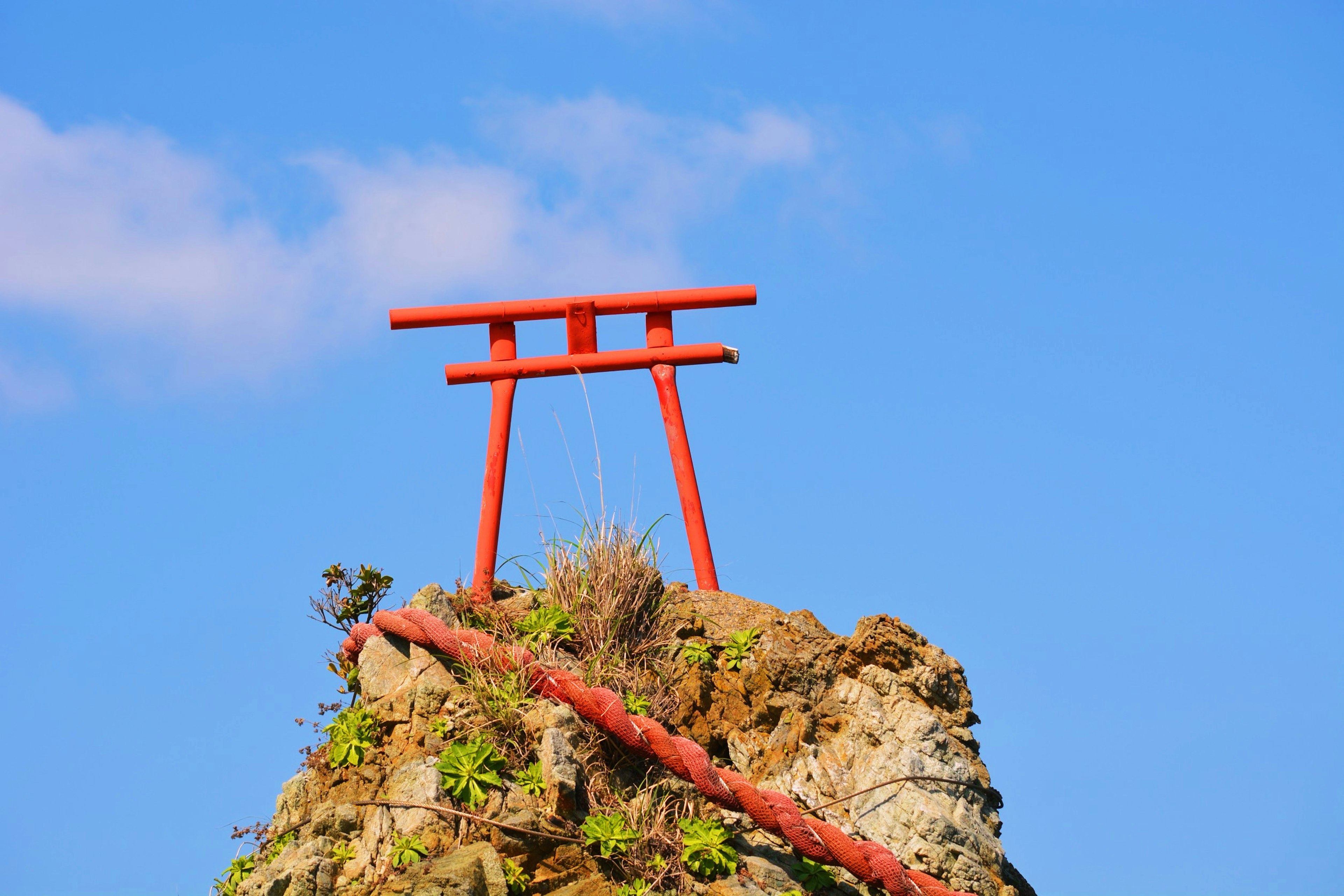 Puerta torii roja sobre una roca con cielo azul