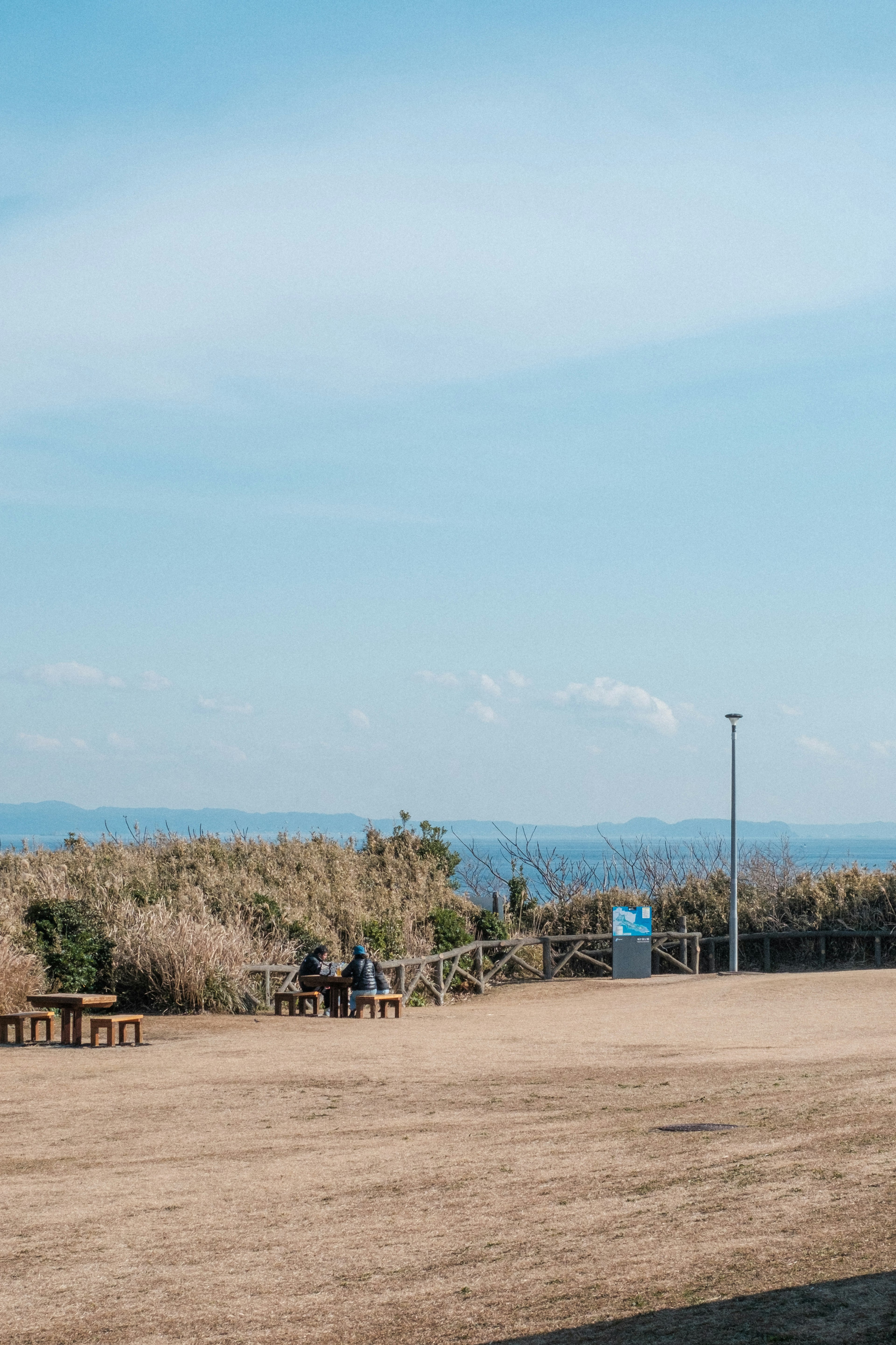 A vast grassy area under a blue sky with benches and a person sitting