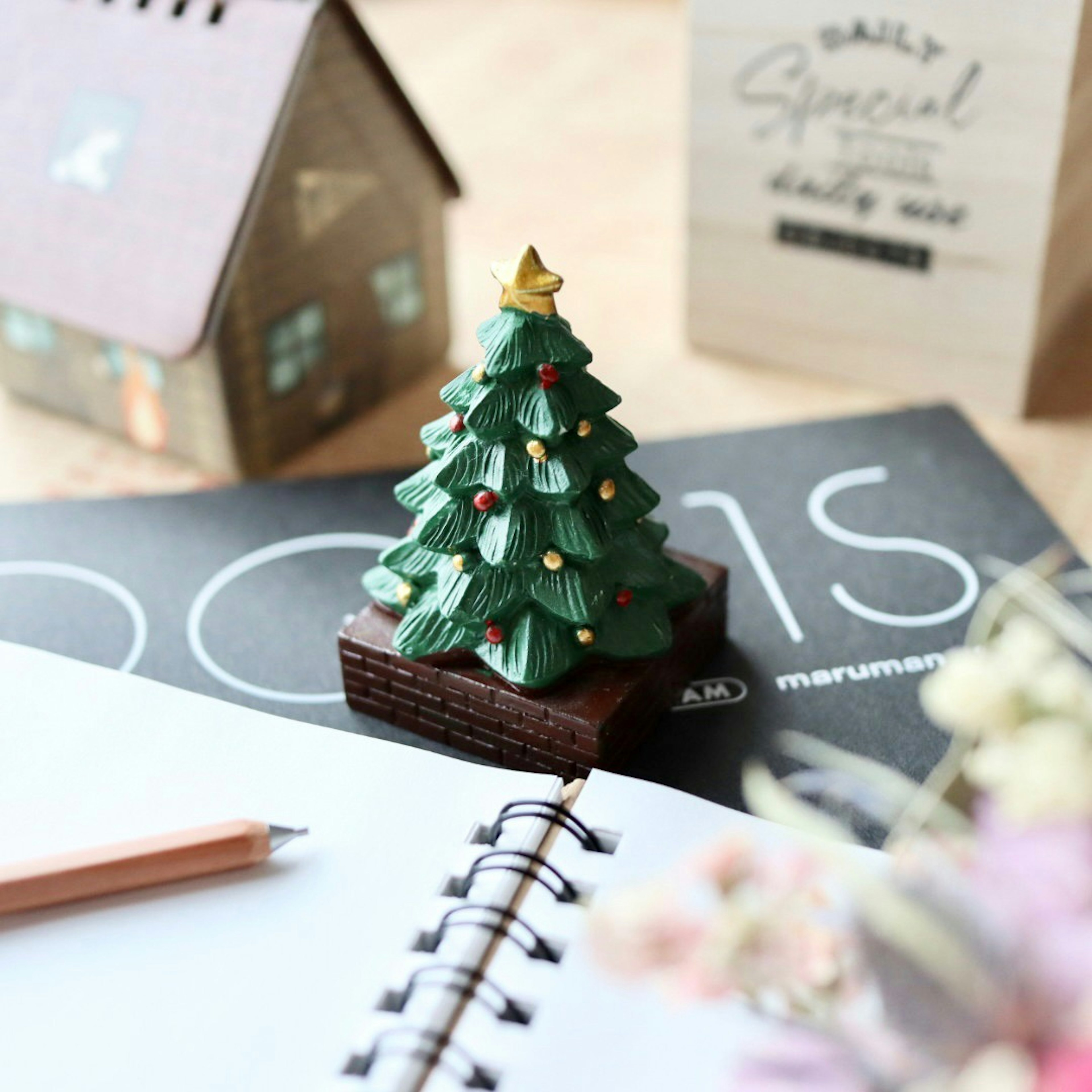 A green Christmas tree figurine placed on a notebook with a pencil and decorative items