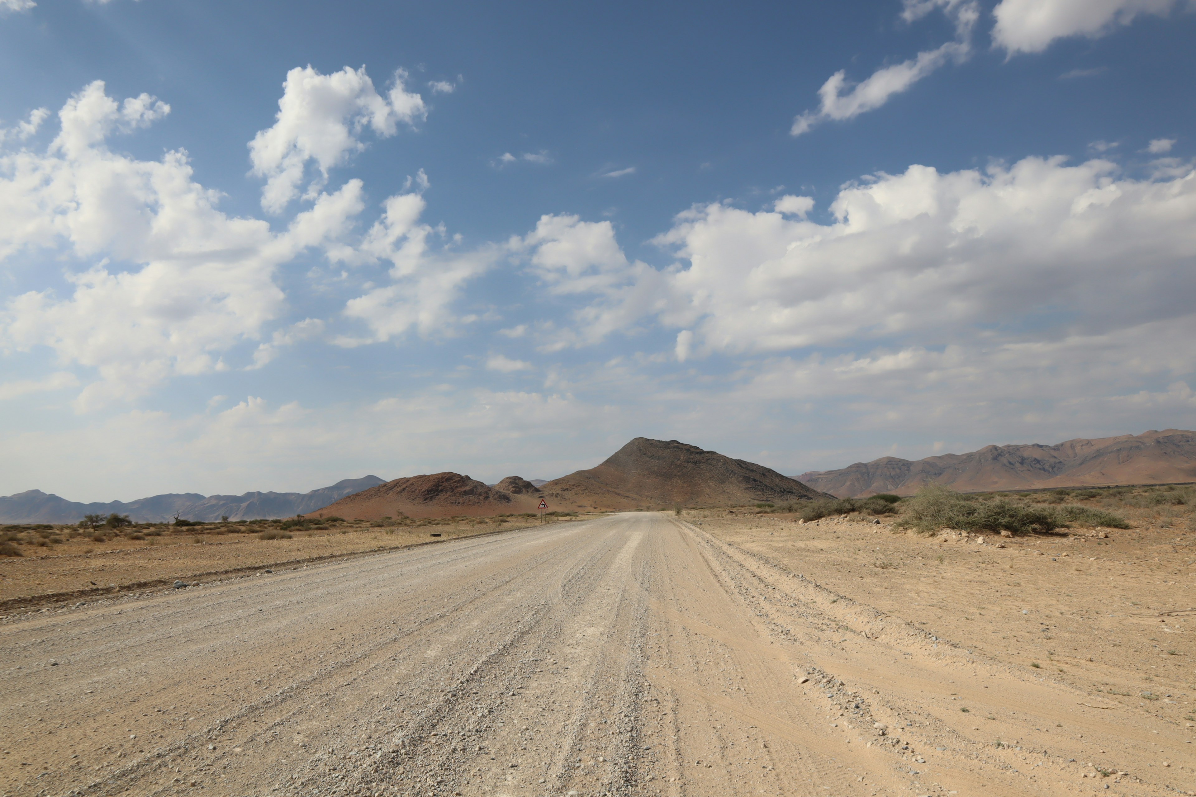 Unbefestigte Straße, die durch eine trockene Wüstenlandschaft mit entfernten Bergen führt