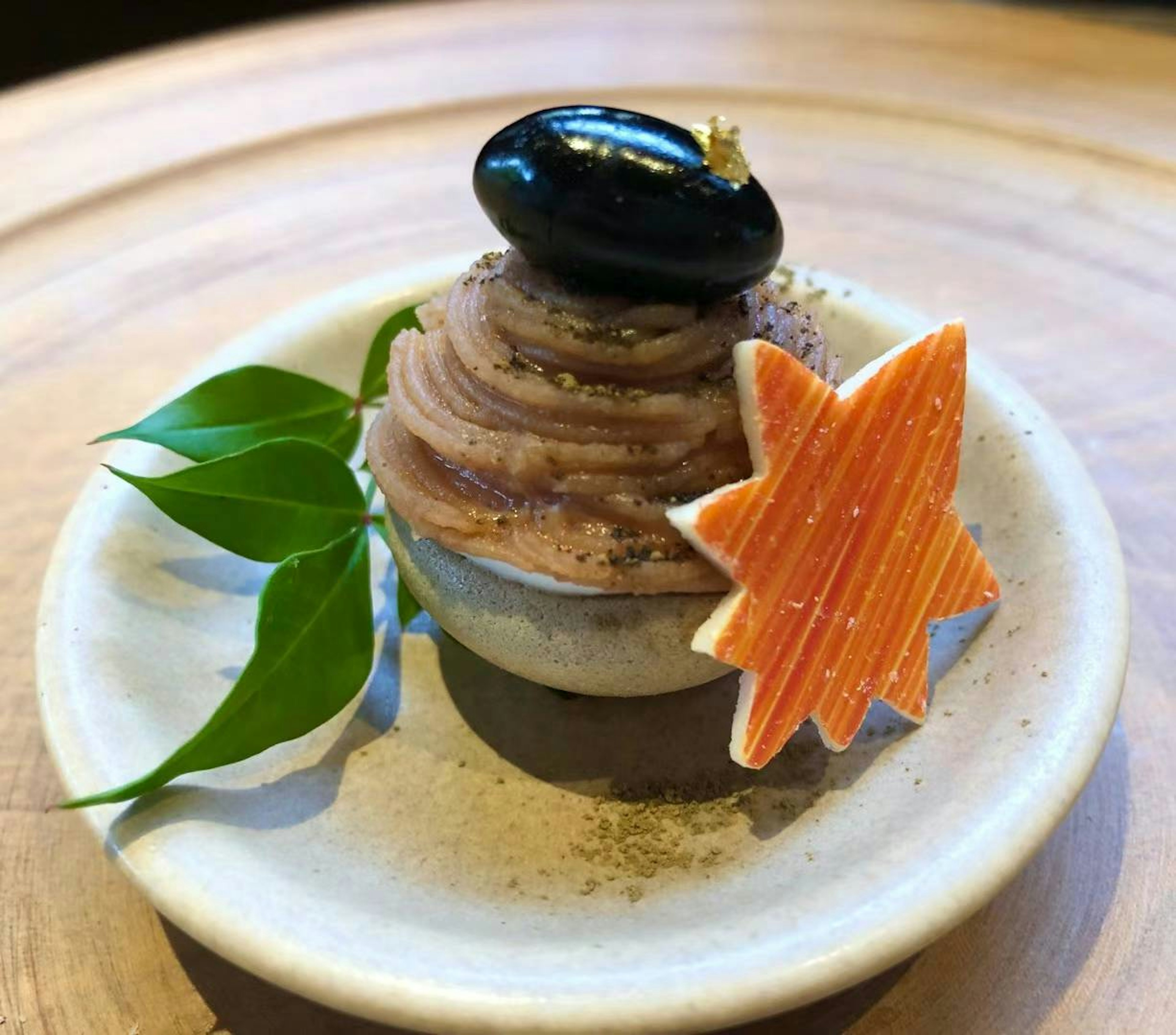 A decorative dessert featuring purple cream topped with a black bean and an orange star-shaped garnish on a small plate