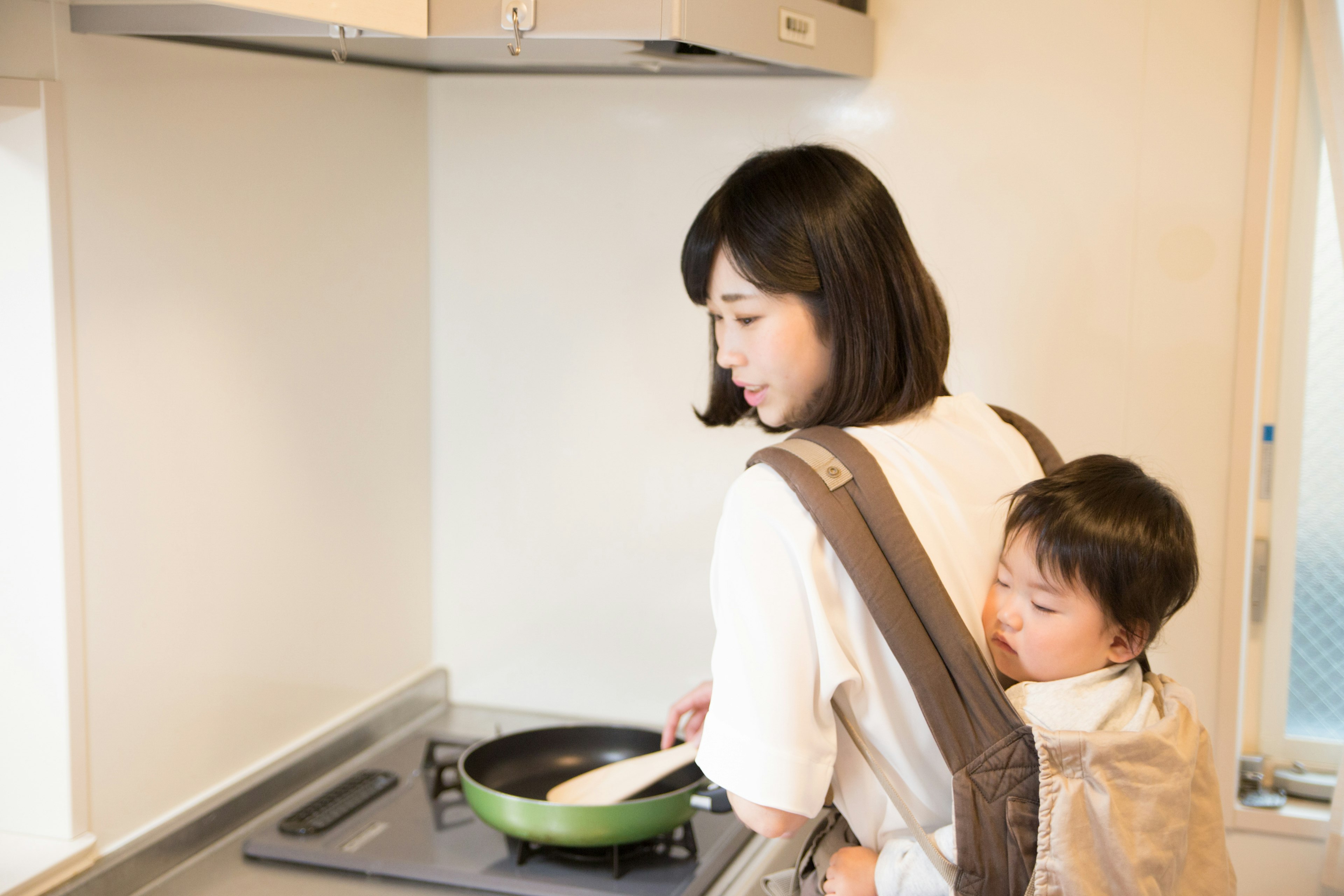 A woman cooking in the kitchen while carrying a baby on her back