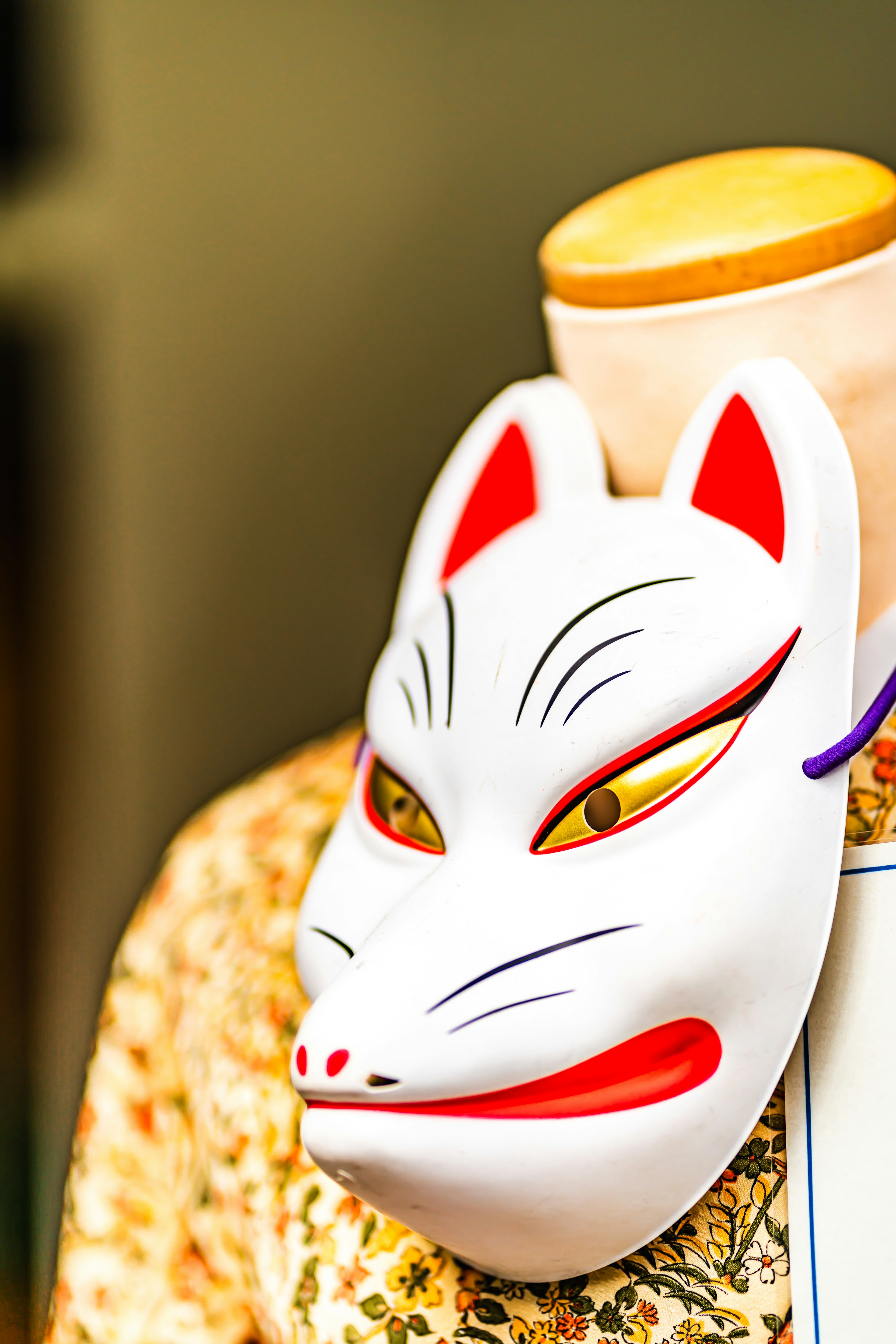 A white fox mask with sharp eyes displayed on a mannequin wearing a floral garment